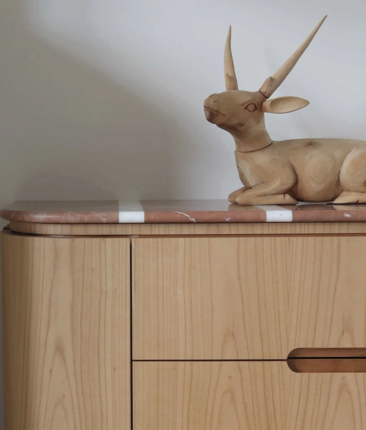 Statue en bois d'un animal ressemblant à un cerf avec de grandes cornes pointues, posé sur une surface en bois.