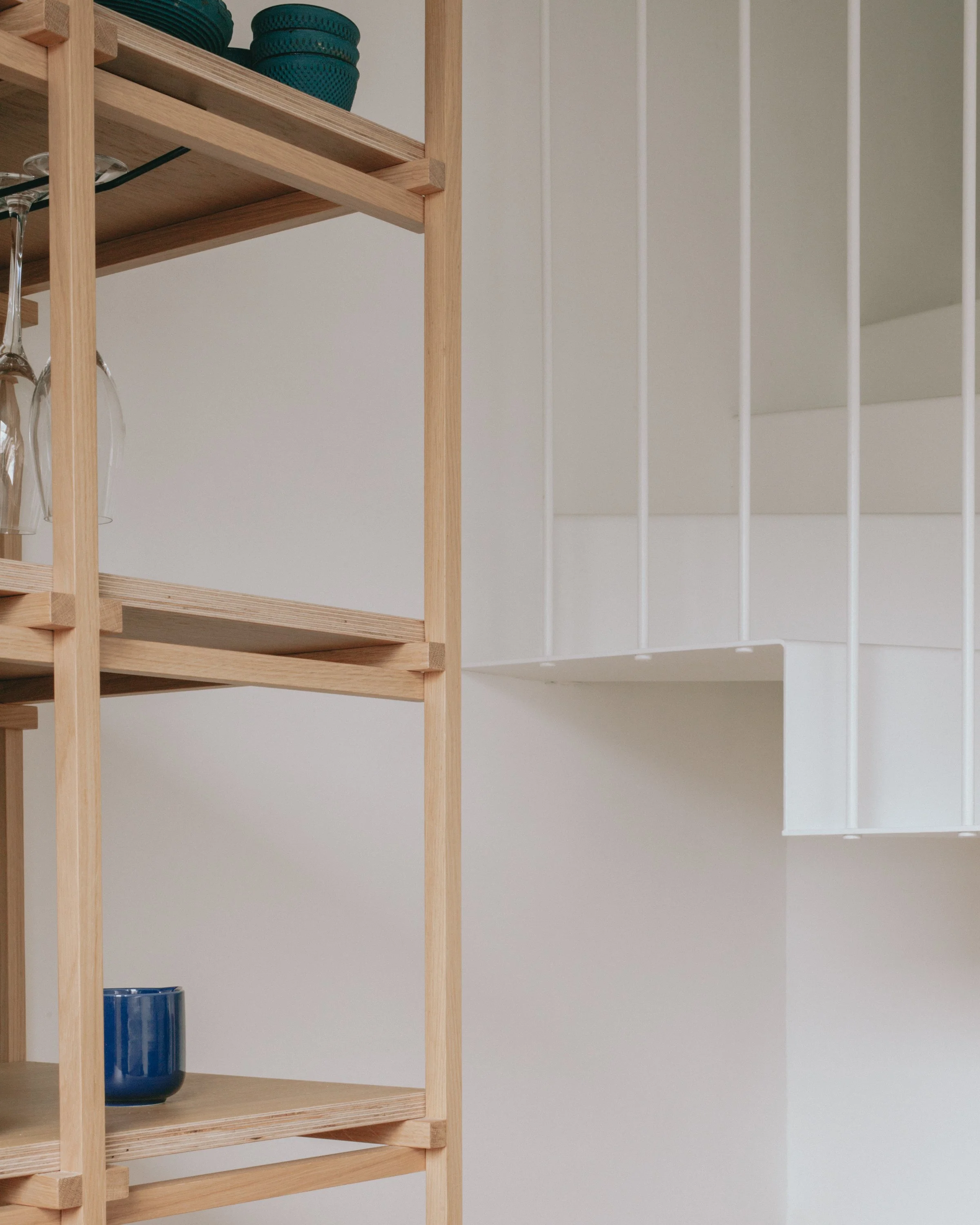 Étagère en bois avec des assiettes bleues, verres à vin et une vase bleue dans un intérieur moderne minimaliste.