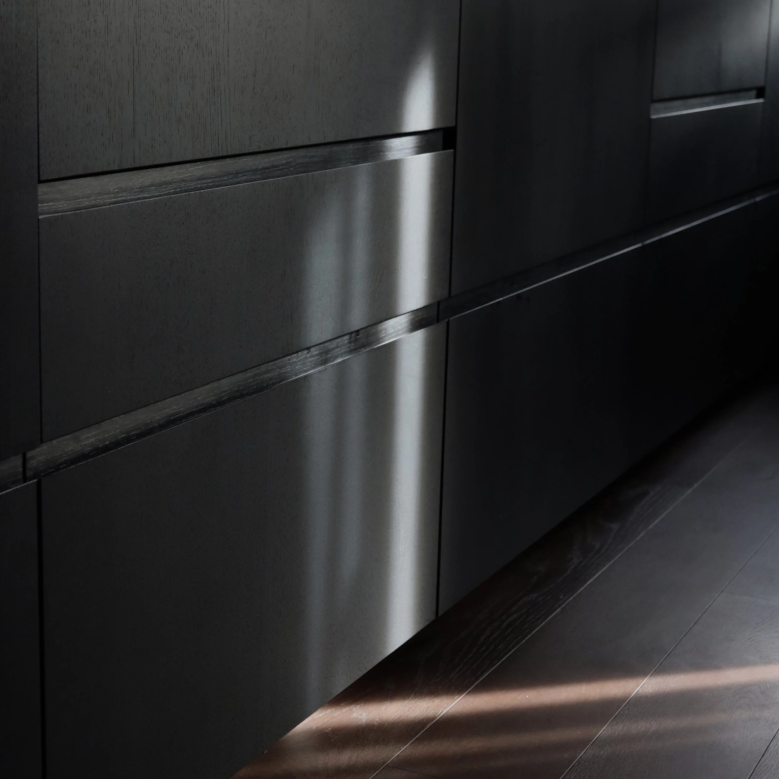 Les portes d’un ascenseur en métal noir avec une lumière naturelle se reflétant, créant un contraste entre l’obscurité et la lumière dans le hall.
