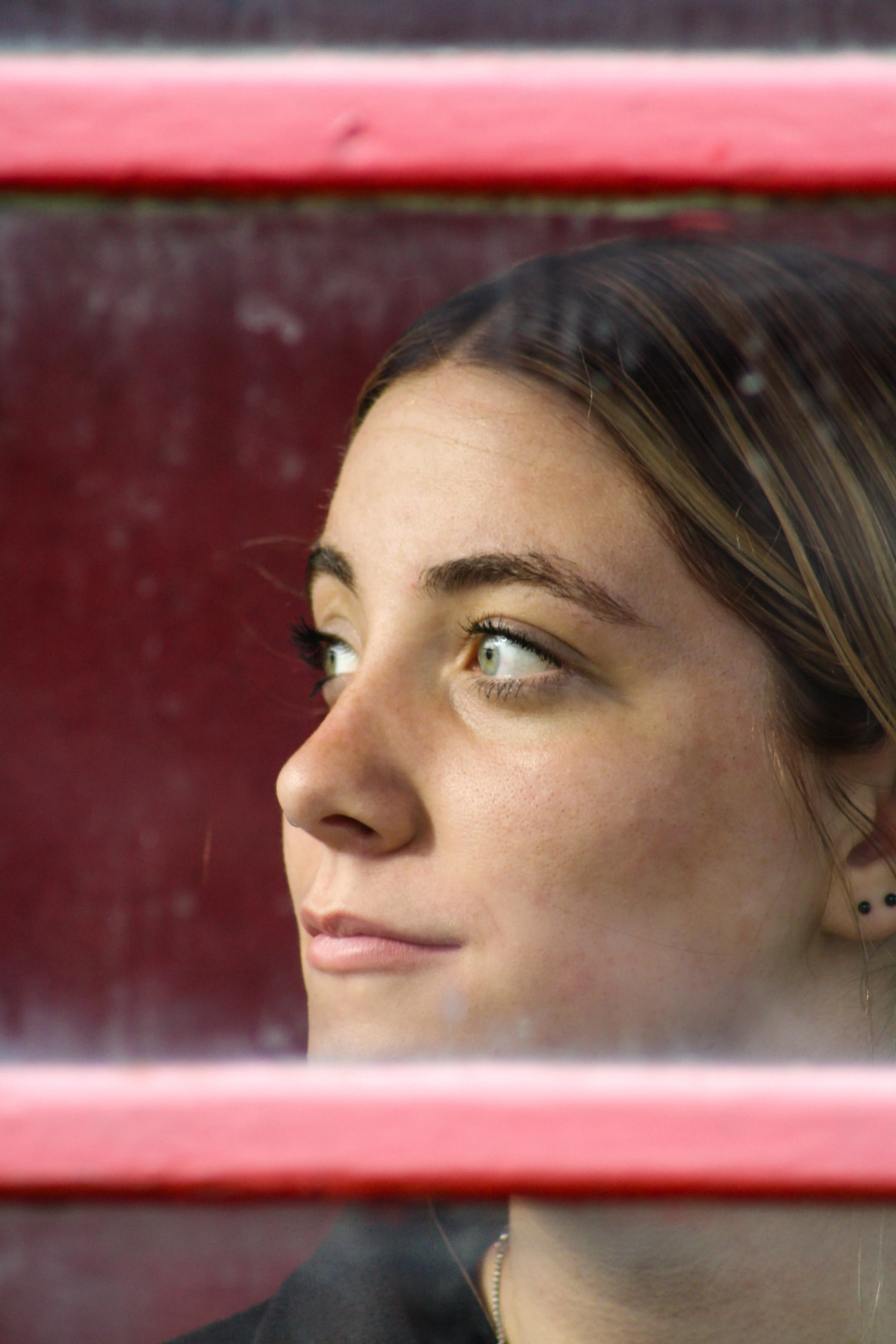 Close-up of a woman with brown hair and green eyes, framed by pink horizontal bars.