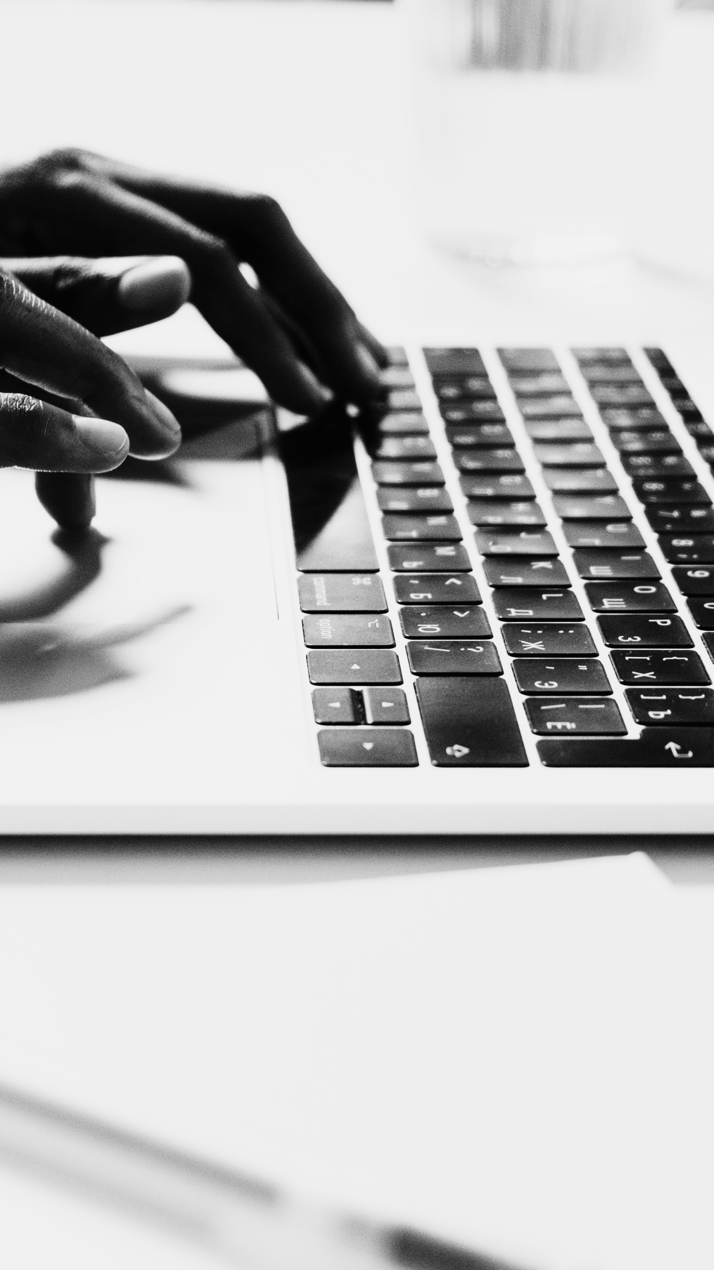 Schwarz-weiße Nahaufnahme einer Person, die auf einer Laptop-Tastatur tippt, mit dem Fokus auf die Hände.