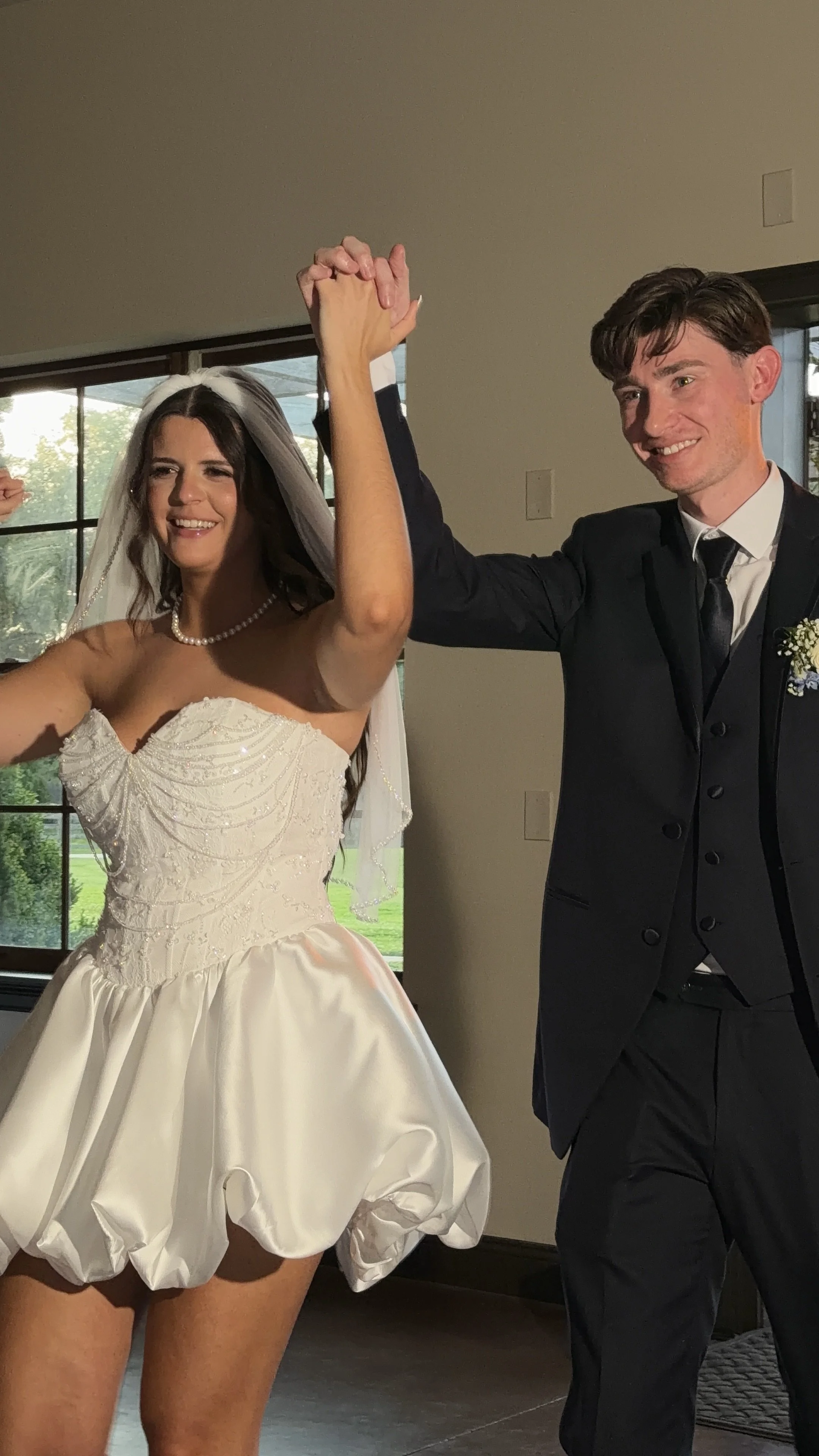 A bride and groom dancing at their wedding reception, holding hands up in celebration.