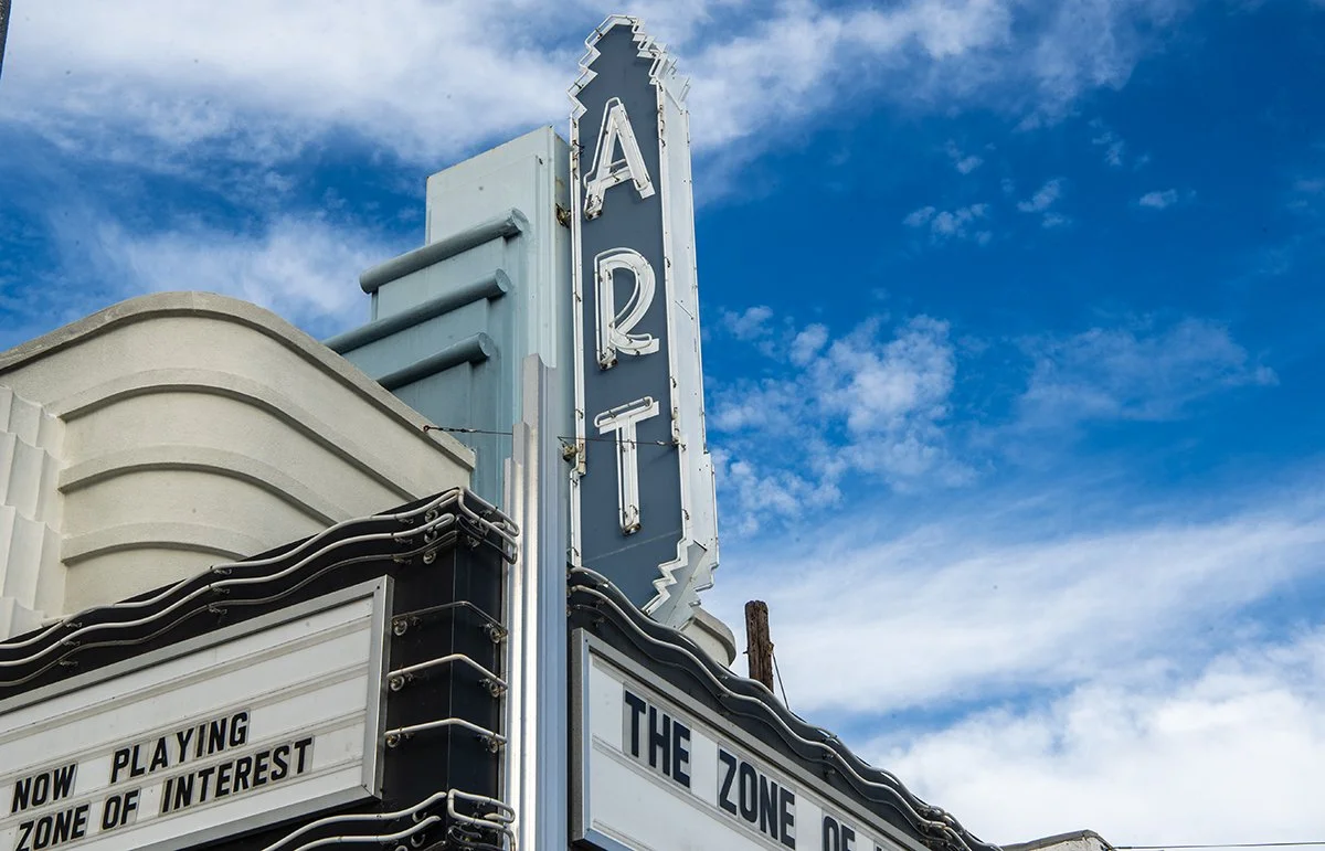 Vintage theater marquee of Art Theatre of Long Beach with a vertical illuminated sign that reads 'ART' against a blue sky with scattered clouds.