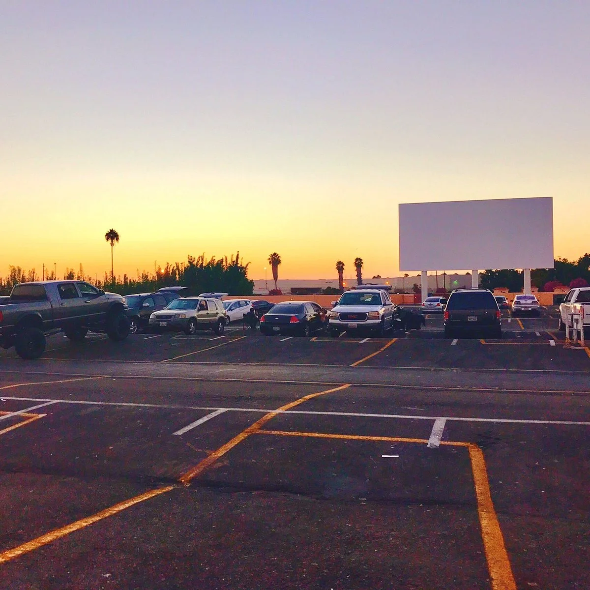 The Paramount Drive-in at sunset with several parked cars, palm trees and a clear sky.
