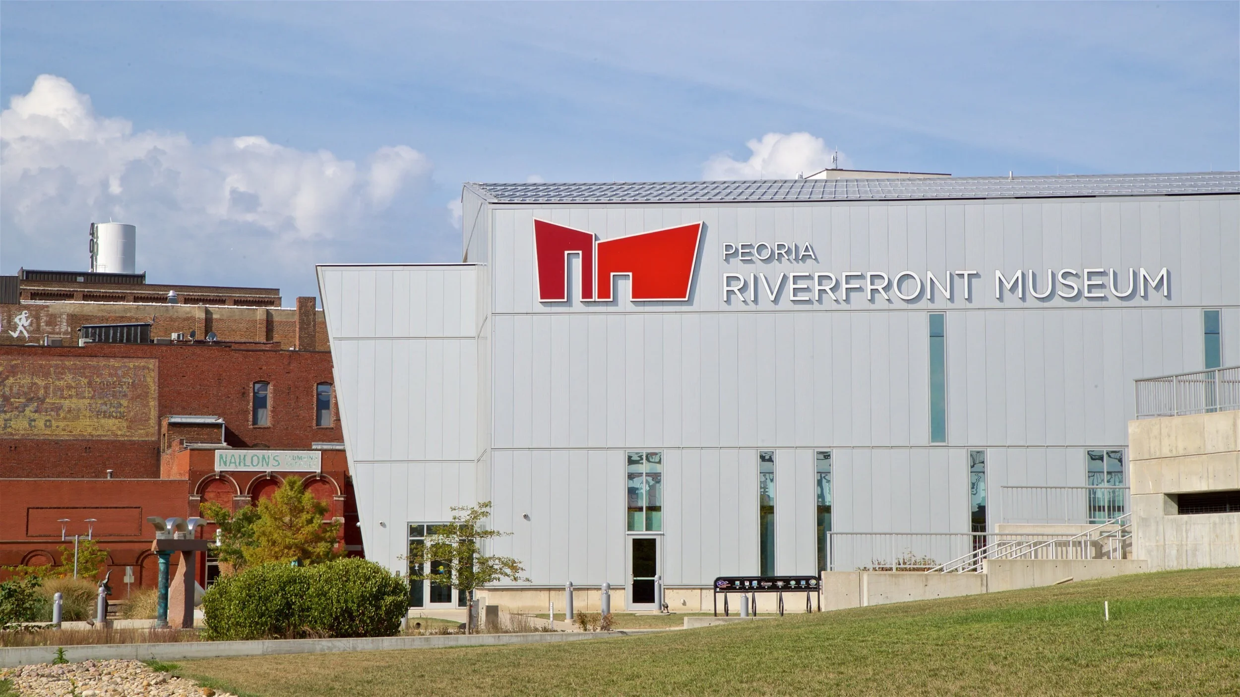 Exterior of the Peoria Riverfront Museum with modern white and red signage, set against a partly cloudy sky.