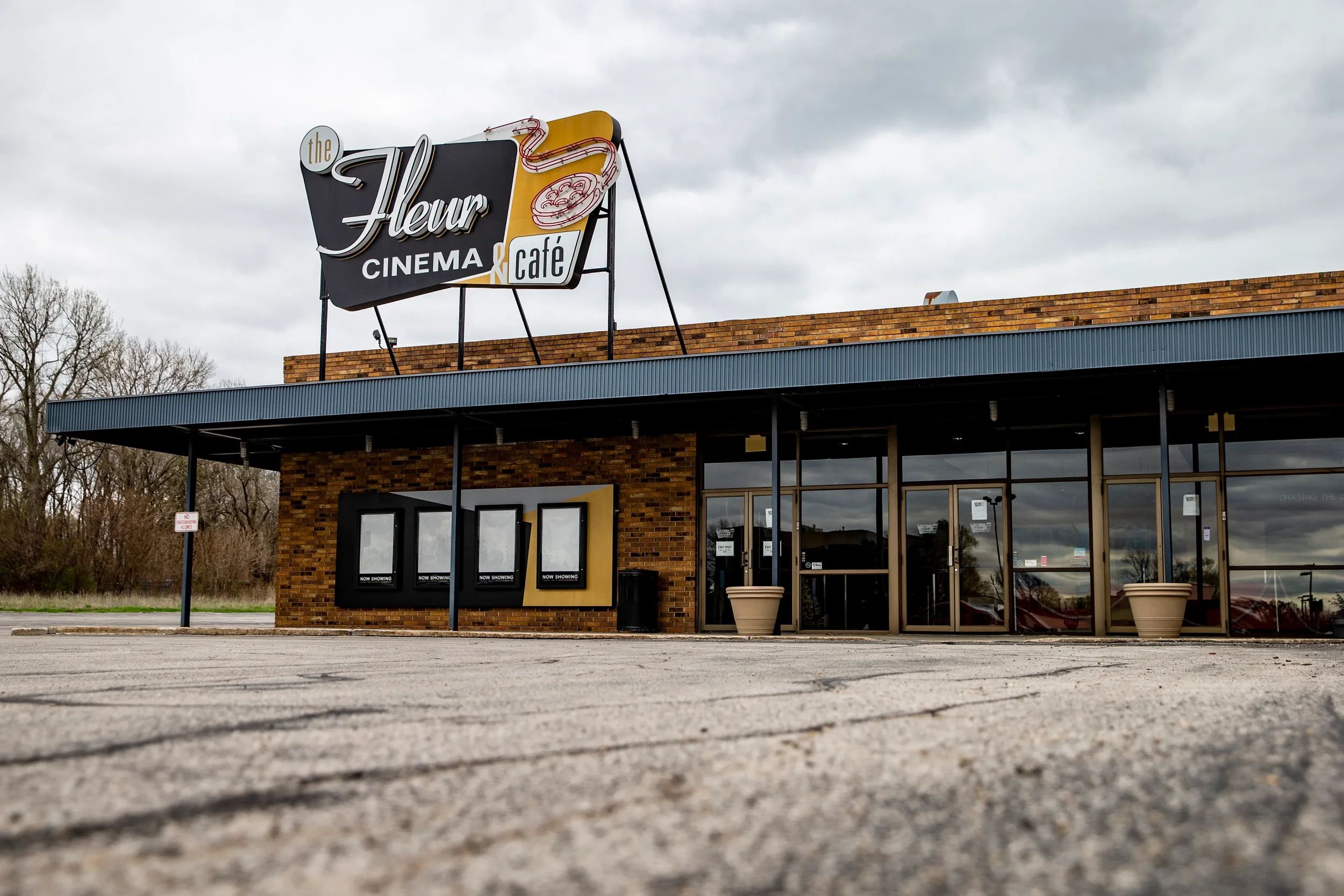 Exterior of a building with a sign that reads 'The Fleur Cinema & Cafe,' featuring a vintage style with a yellow and black color scheme and a pizza slice graphic.
