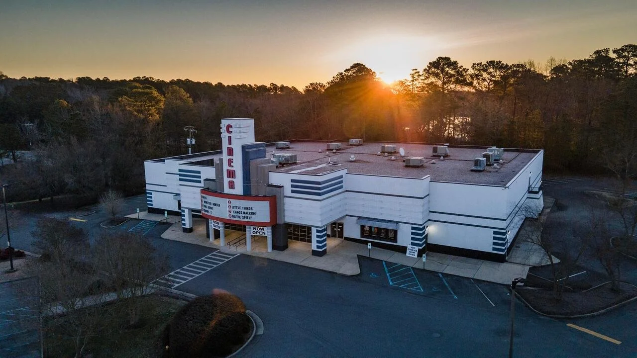 York River Crossing Cinemas, the marquee sign says 'NOW OPEN' at sunset, surrounded by the parking lot and trees in the background.