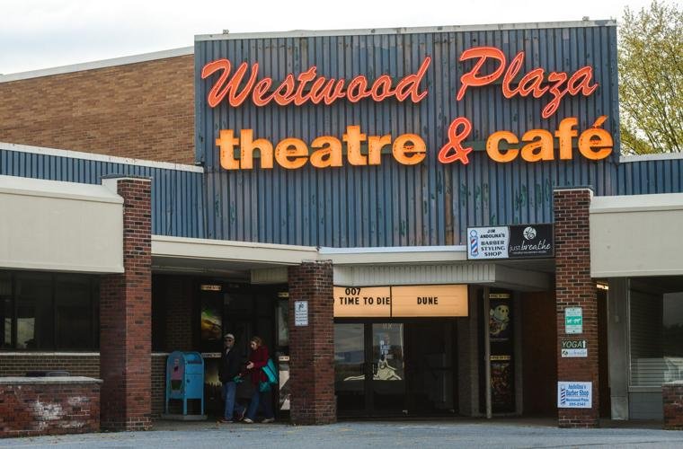 Exterior view of Westwood Plaza Theatre & Café with a large sign, brick and blue siding, and some people standing near the entrance.