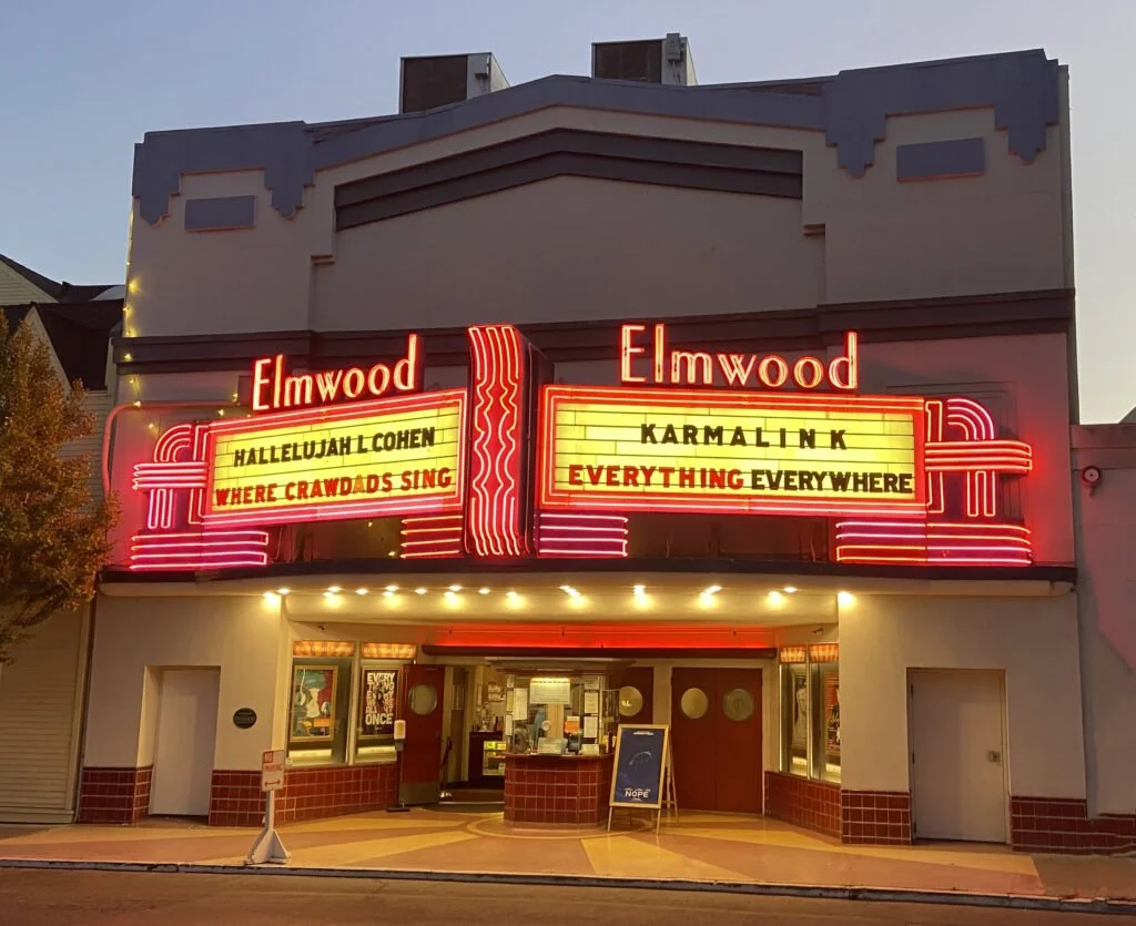 The Elmwood theater showing posters for musical acts, with illuminated signage and marquee displaying song titles.