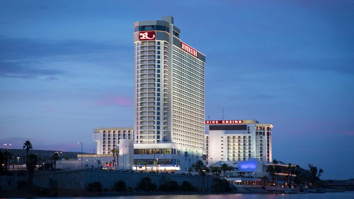 The Riverside Laughlin, a tall modern hotel building, located by water, with a surrounding skyline at dusk.