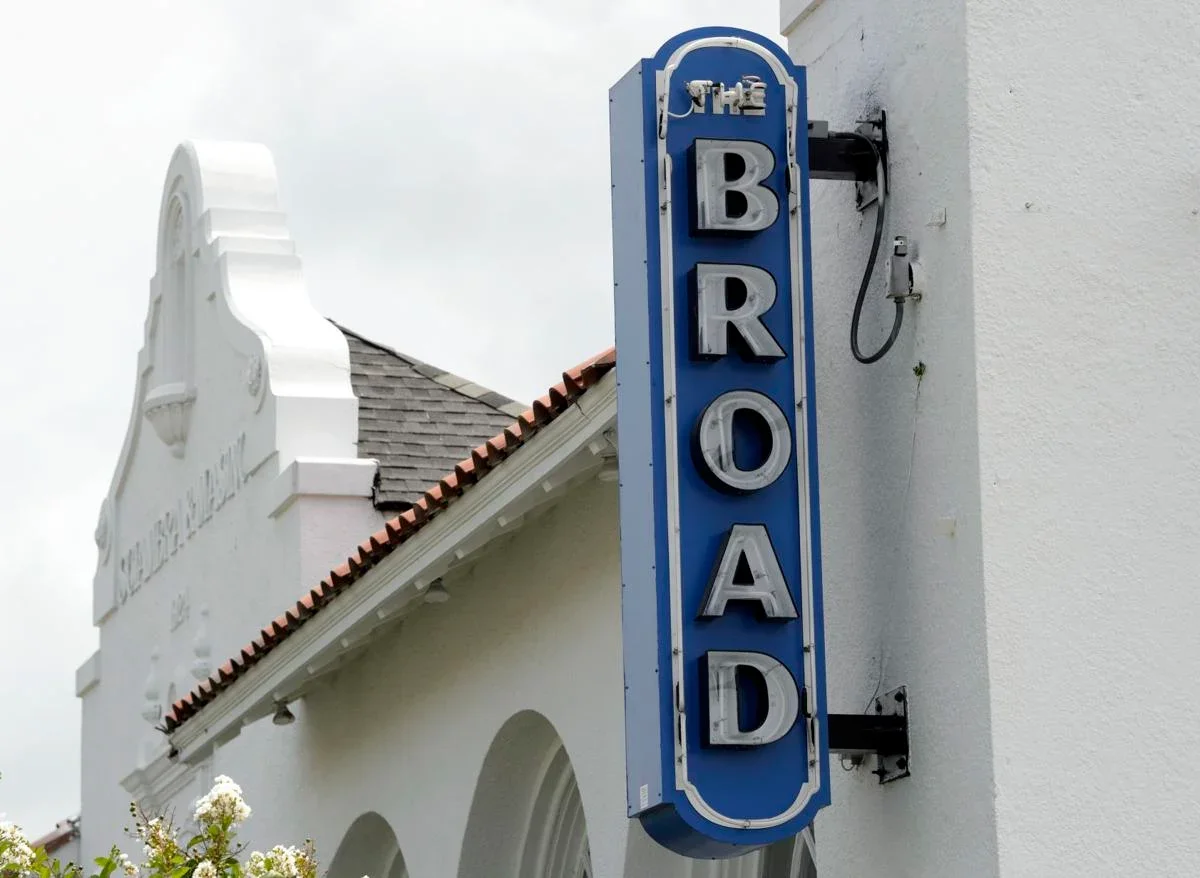 Blue vertical neon sign of The Broad theater, mounted on the white building exterior.