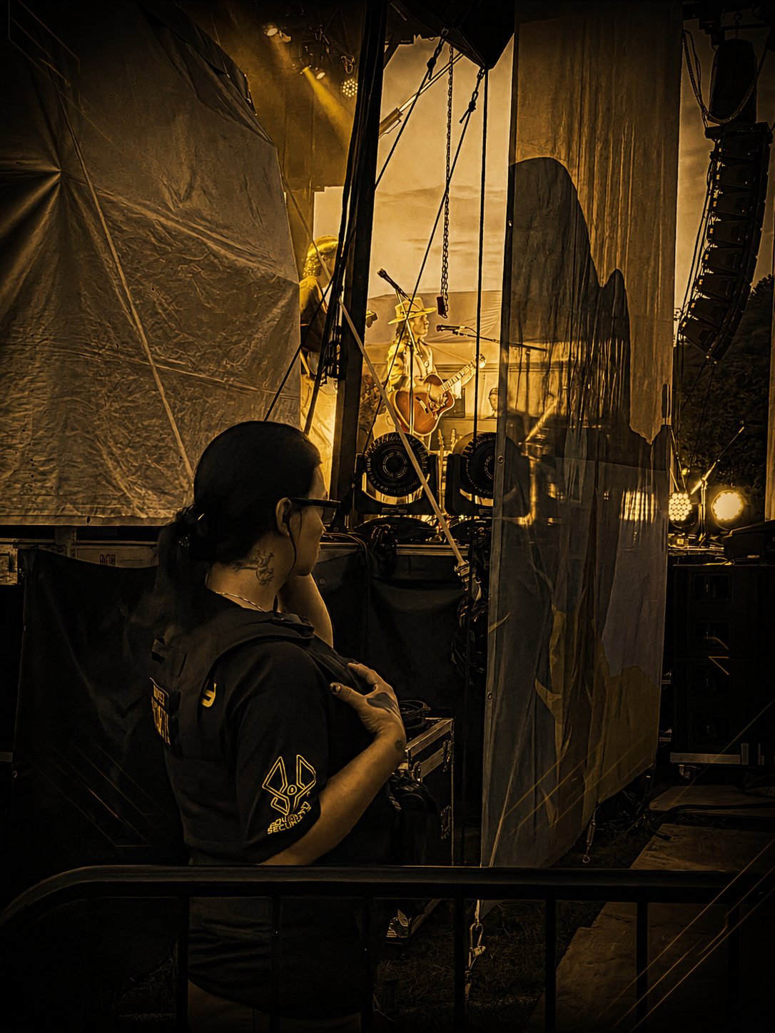 A woman Monarch Security Agent wearing glasses and a Monarch security vest is watching the crowd at a live music performance on stage.