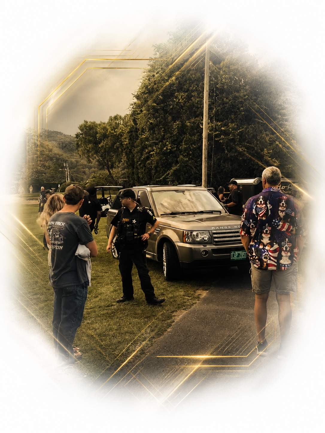 A monarch security officer talking to a person near a Range Rover car during an outdoor event with several people in the background, trees, and a cloudy sky.