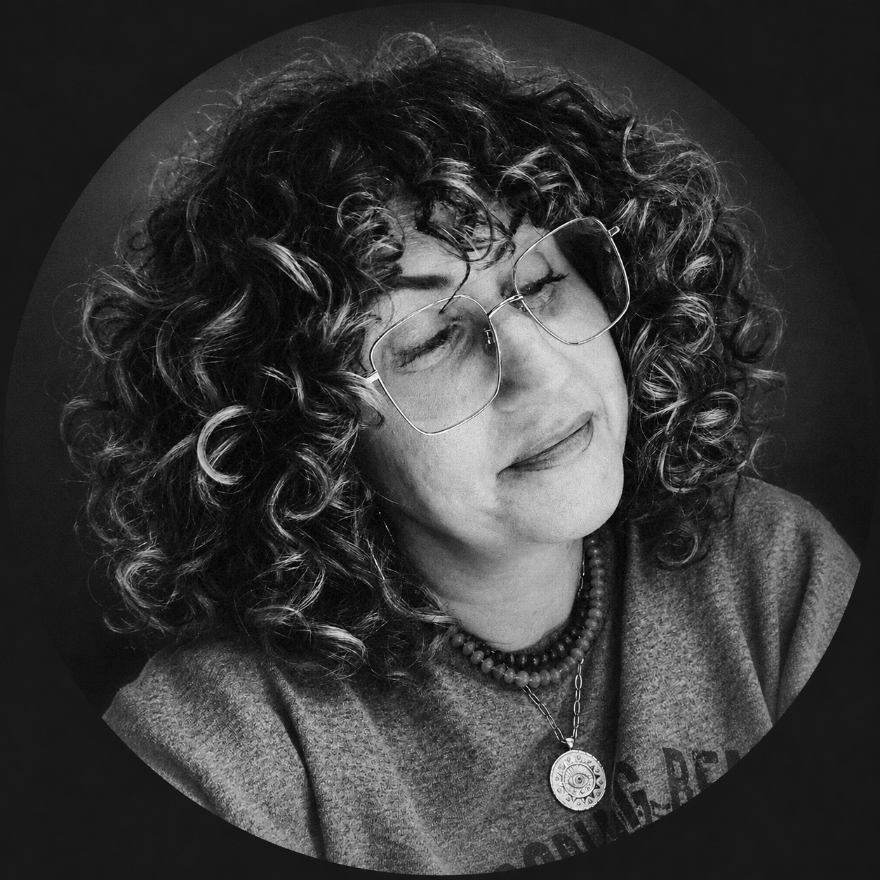Black-and-white portrait of a woman with curly hair and glasses, smiling softly.