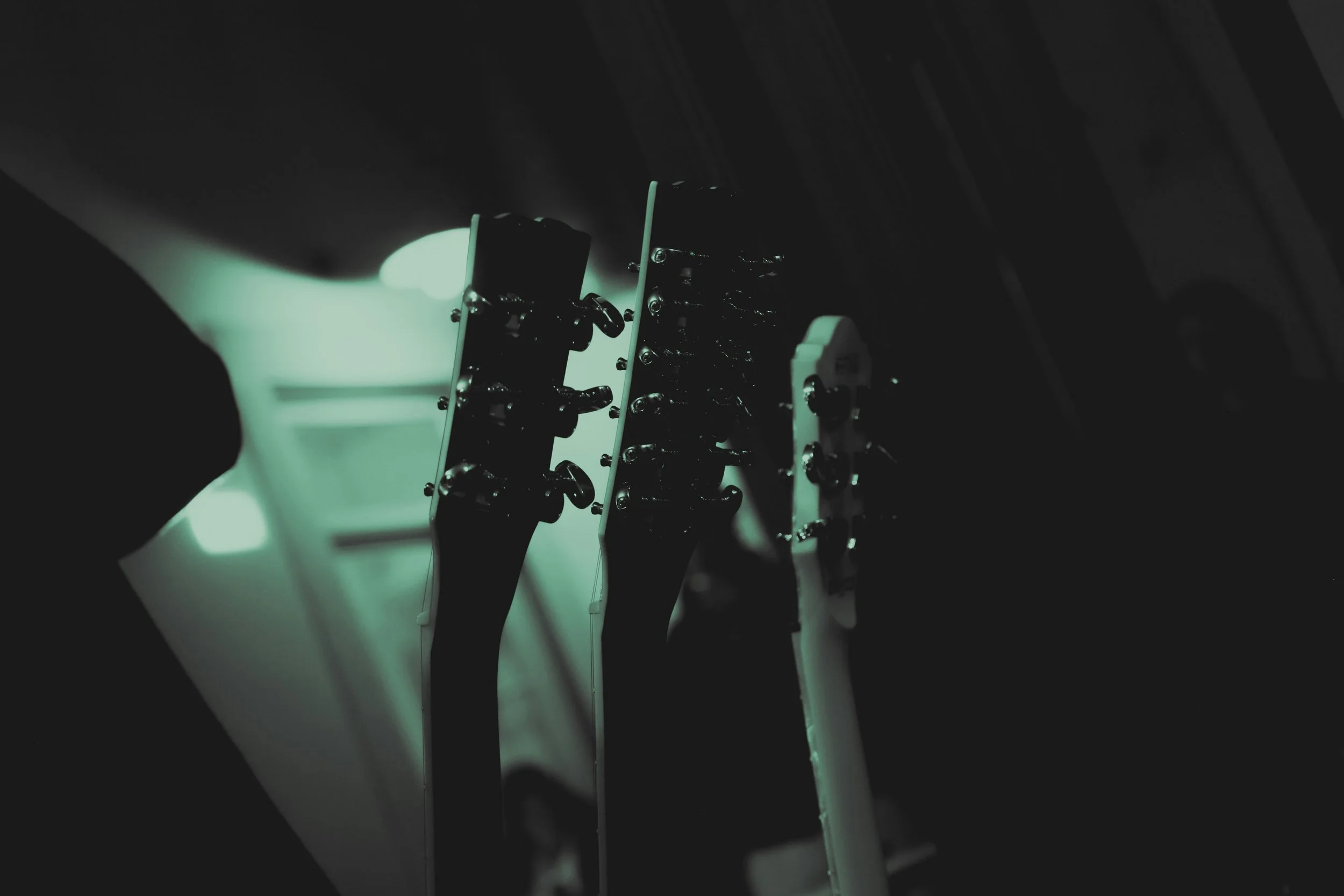 Close-up of an electric guitar's headstock, tuning pegs, and strings, with a dark background.