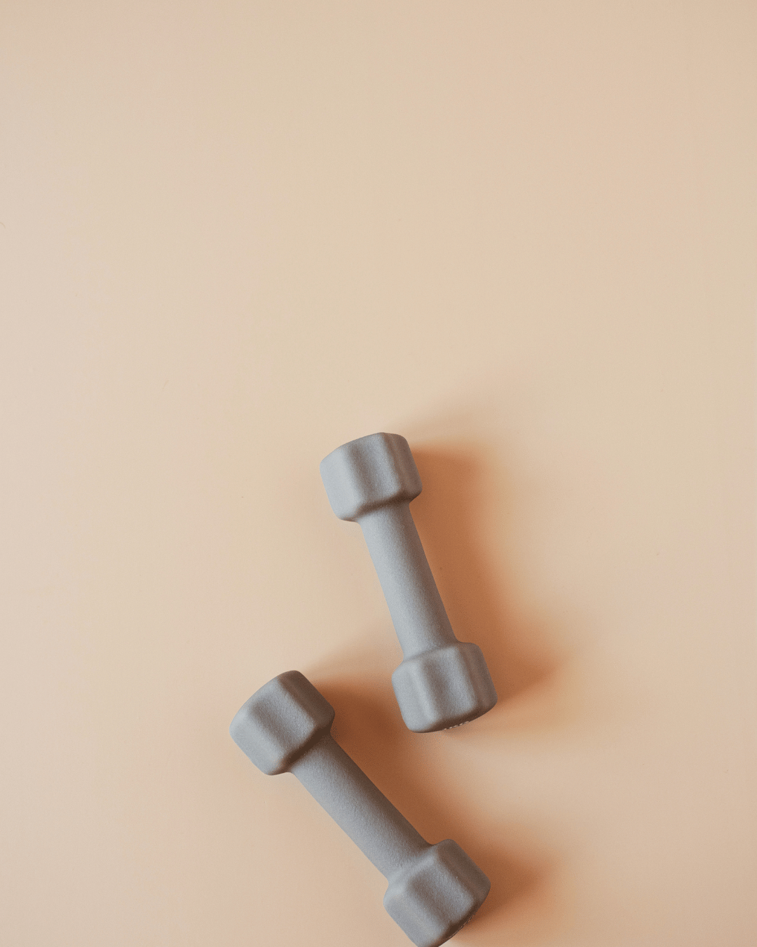 Gray dumbbells placed on a light peach background.
