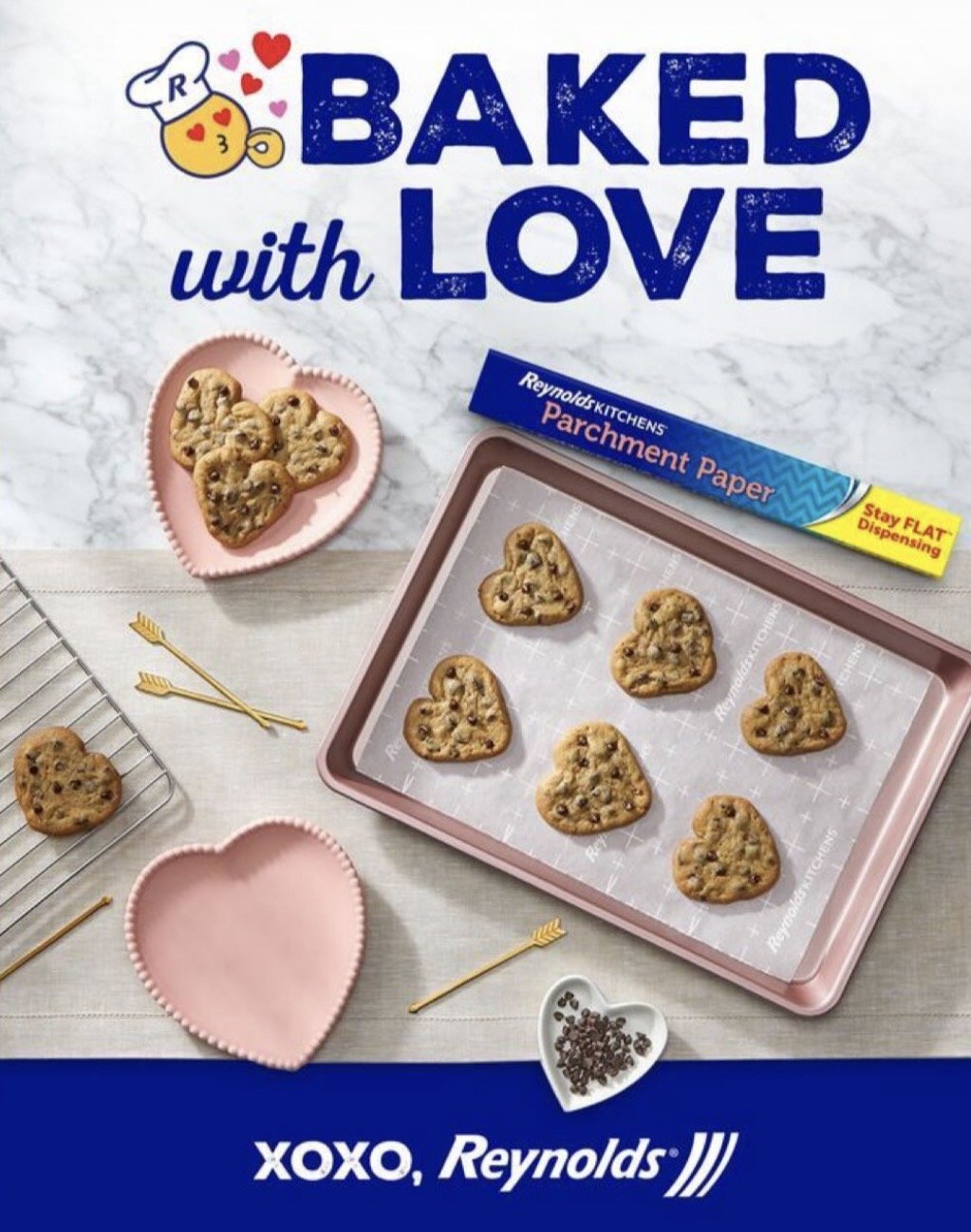 A baking scene with heart-shaped chocolate chip cookies on a pink baking sheet and on a cooling rack, surrounded by pink heart-shaped bowls, gold heart skewers, and a box of Reynolds Kitchen parchment paper, with a large text overlay that reads "Bake