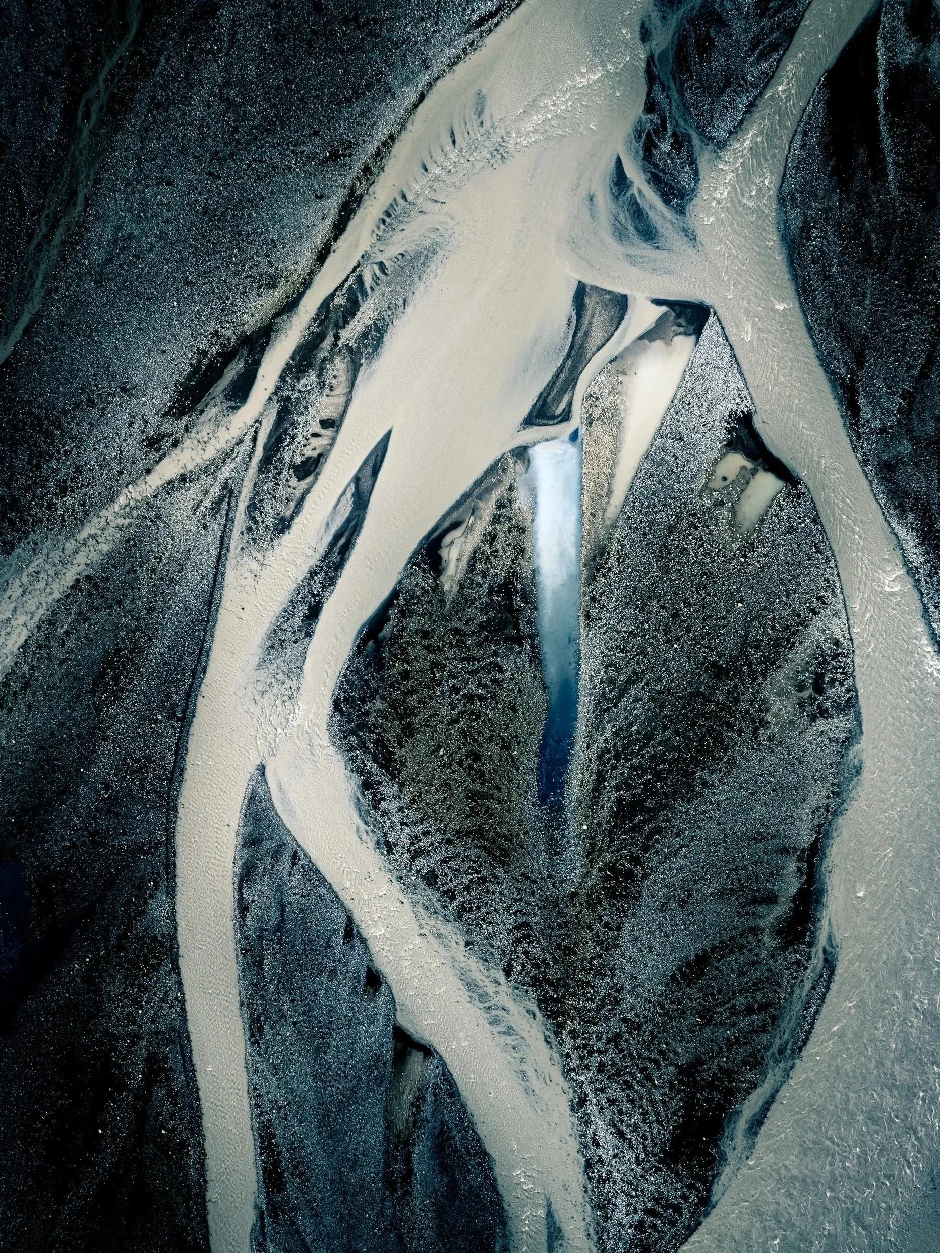 Aerial view of pale glacial sediments forming intricate patterns across dark terrain in Iceland