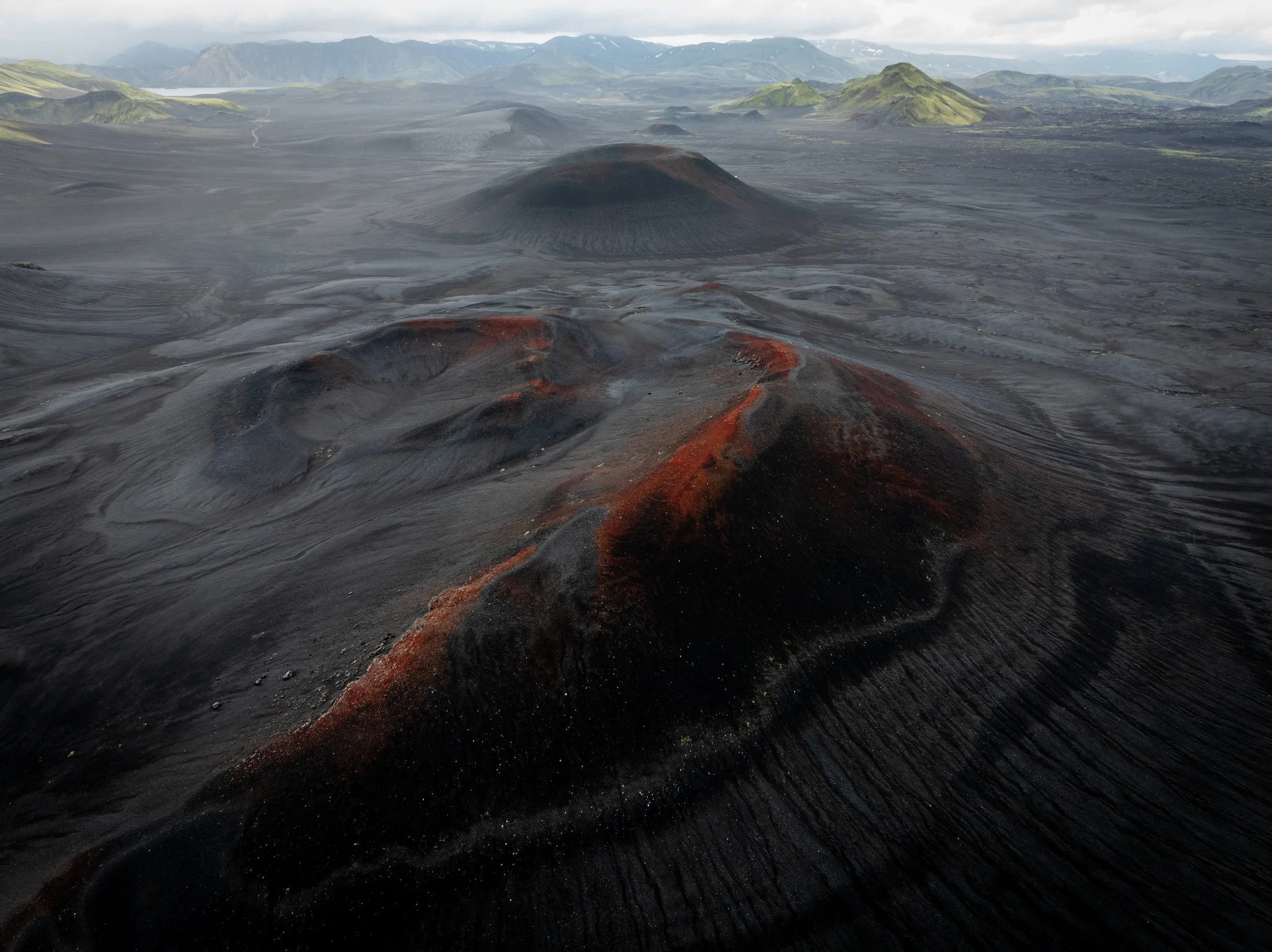 Aerial view of dark volcanic craters and red volcanic slopes in the Icelandic Highlands