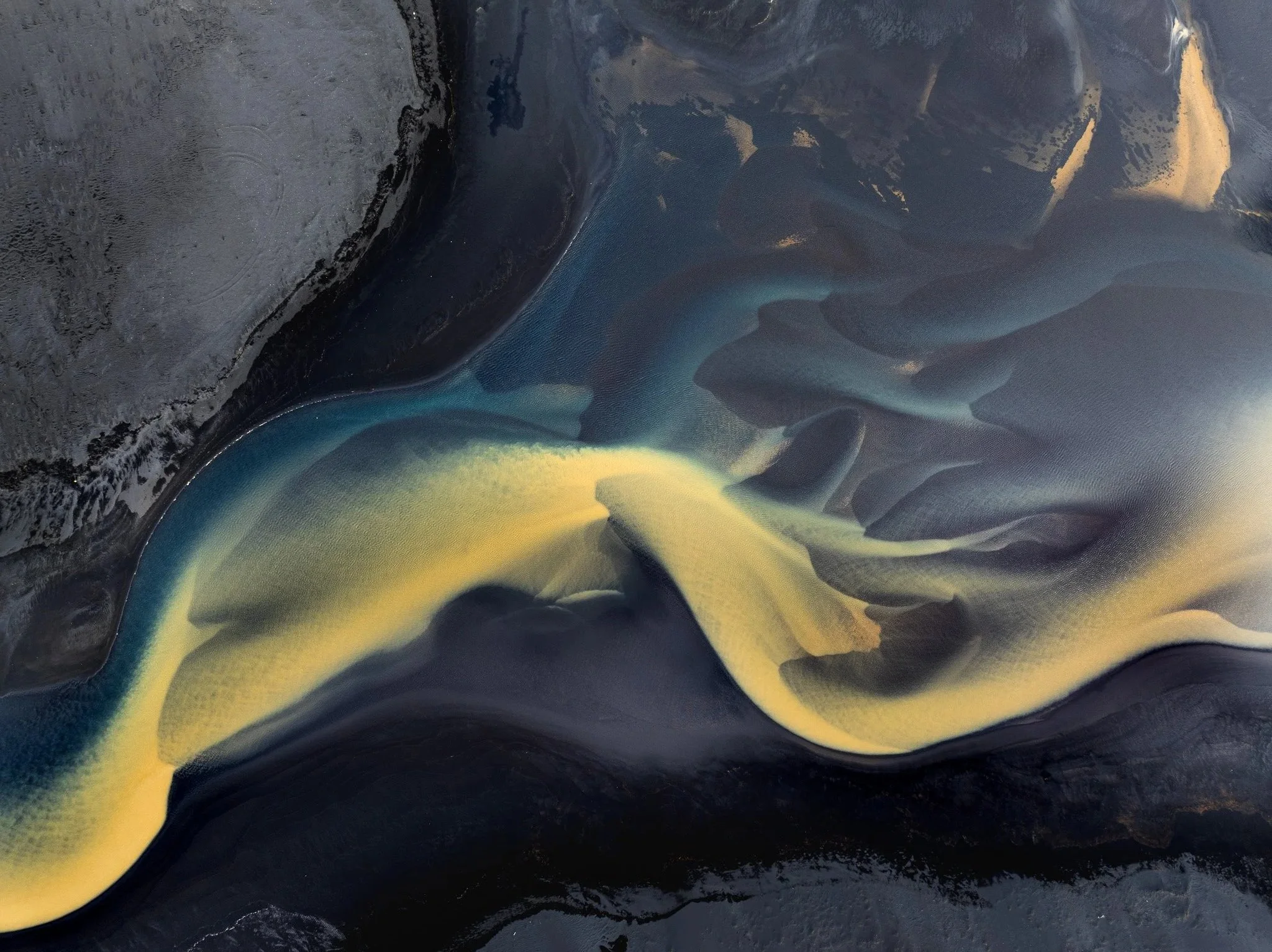 Glacial river channels forming flowing patterns across black volcanic sand in Iceland