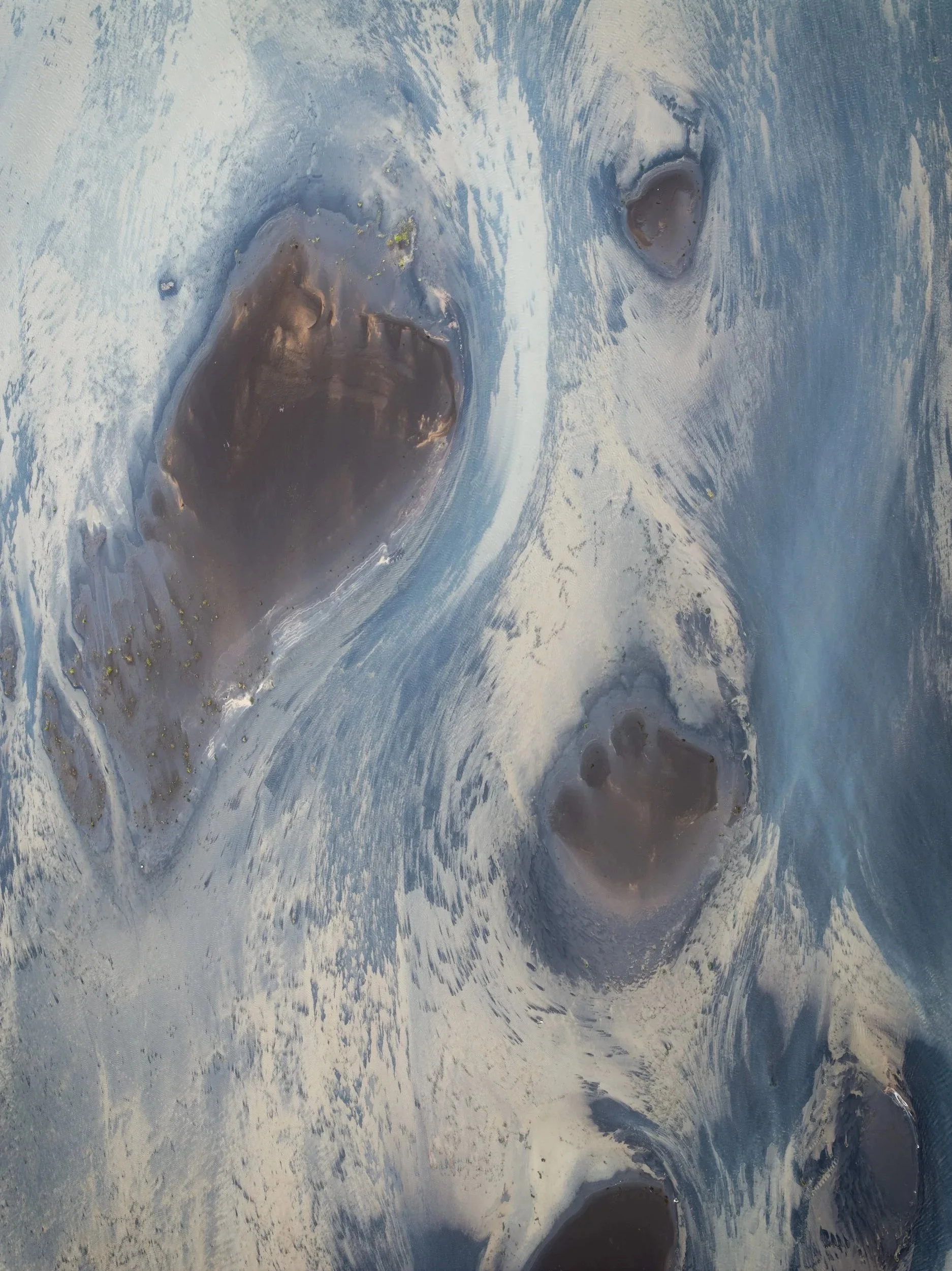 Aerial view of dark glacial sediment surrounded by pale mineral surfaces in Iceland