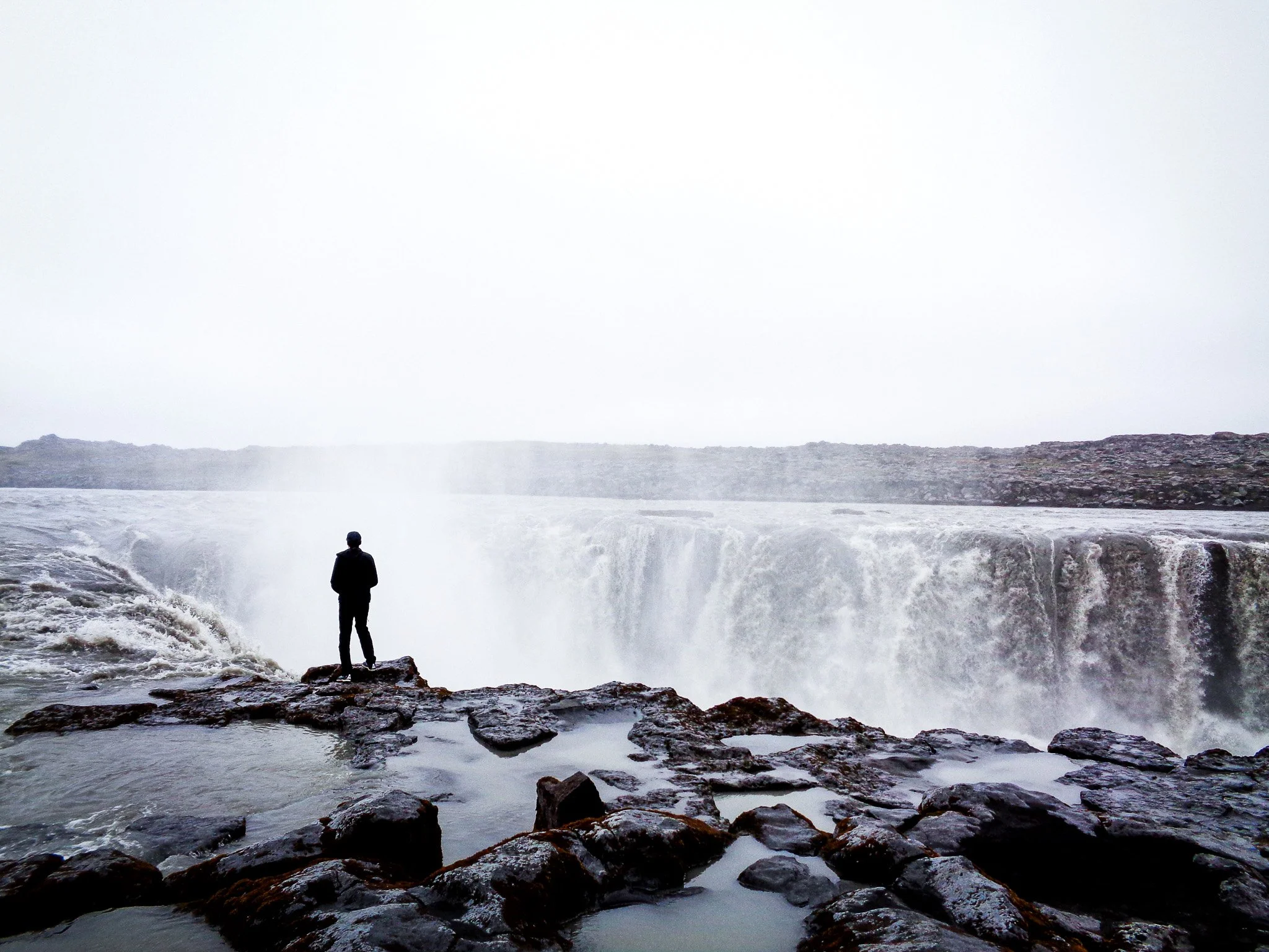 Selfoss waterfall in Iceland with a lone person standing on the rocky edge above the rushing water