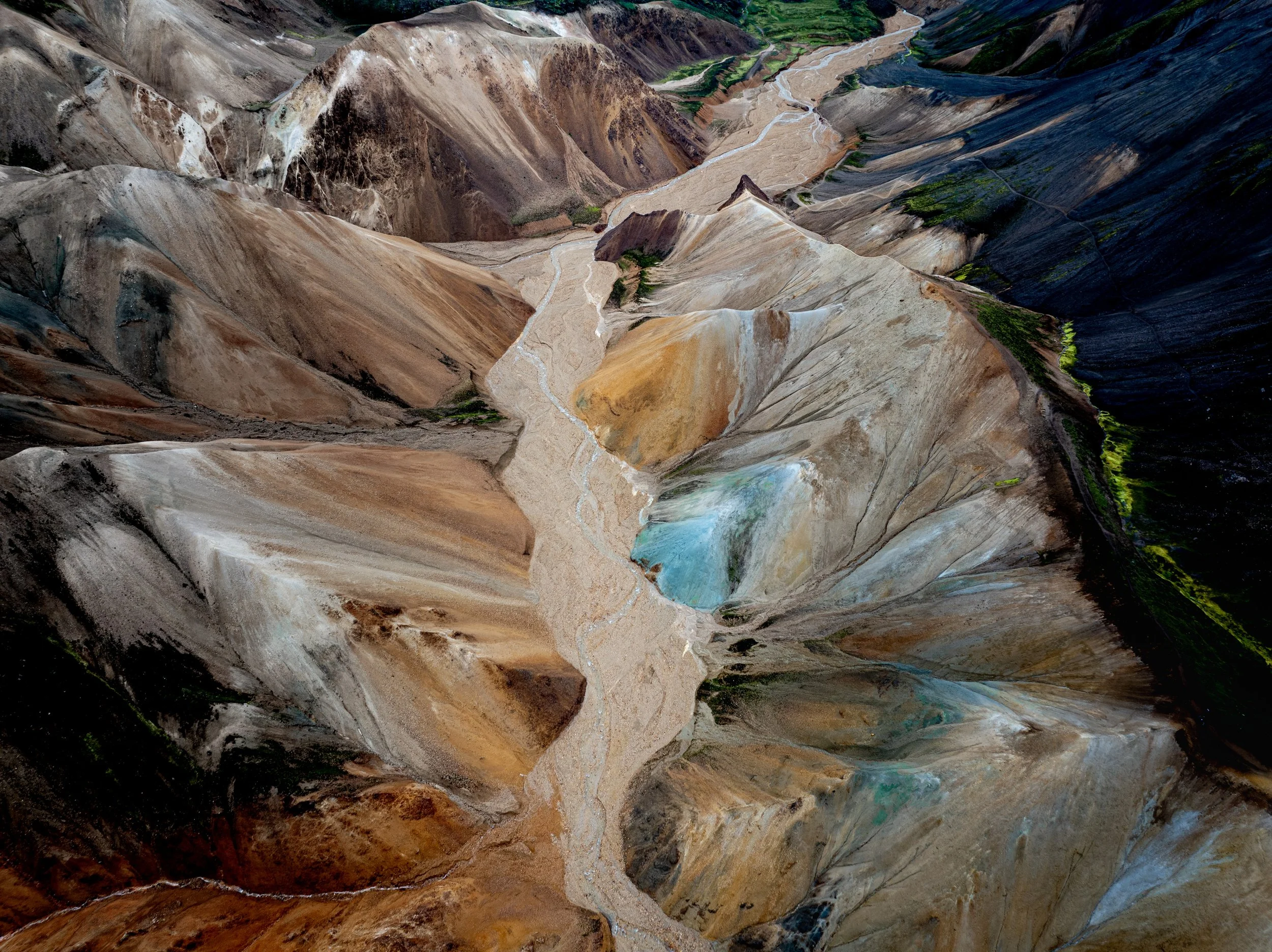 Aerial view of colorful volcanic mountains, geothermal terrain and a winding stream in Landmannalaugar, Iceland