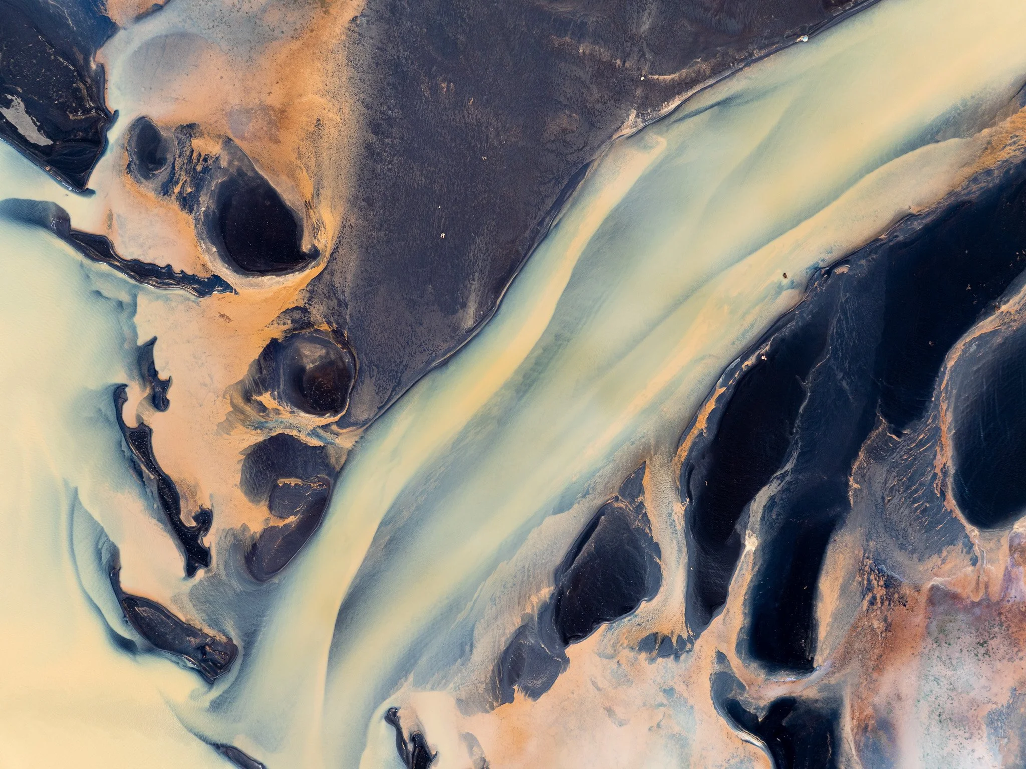 Blue glacial river channels winding through dark volcanic sand in Iceland
