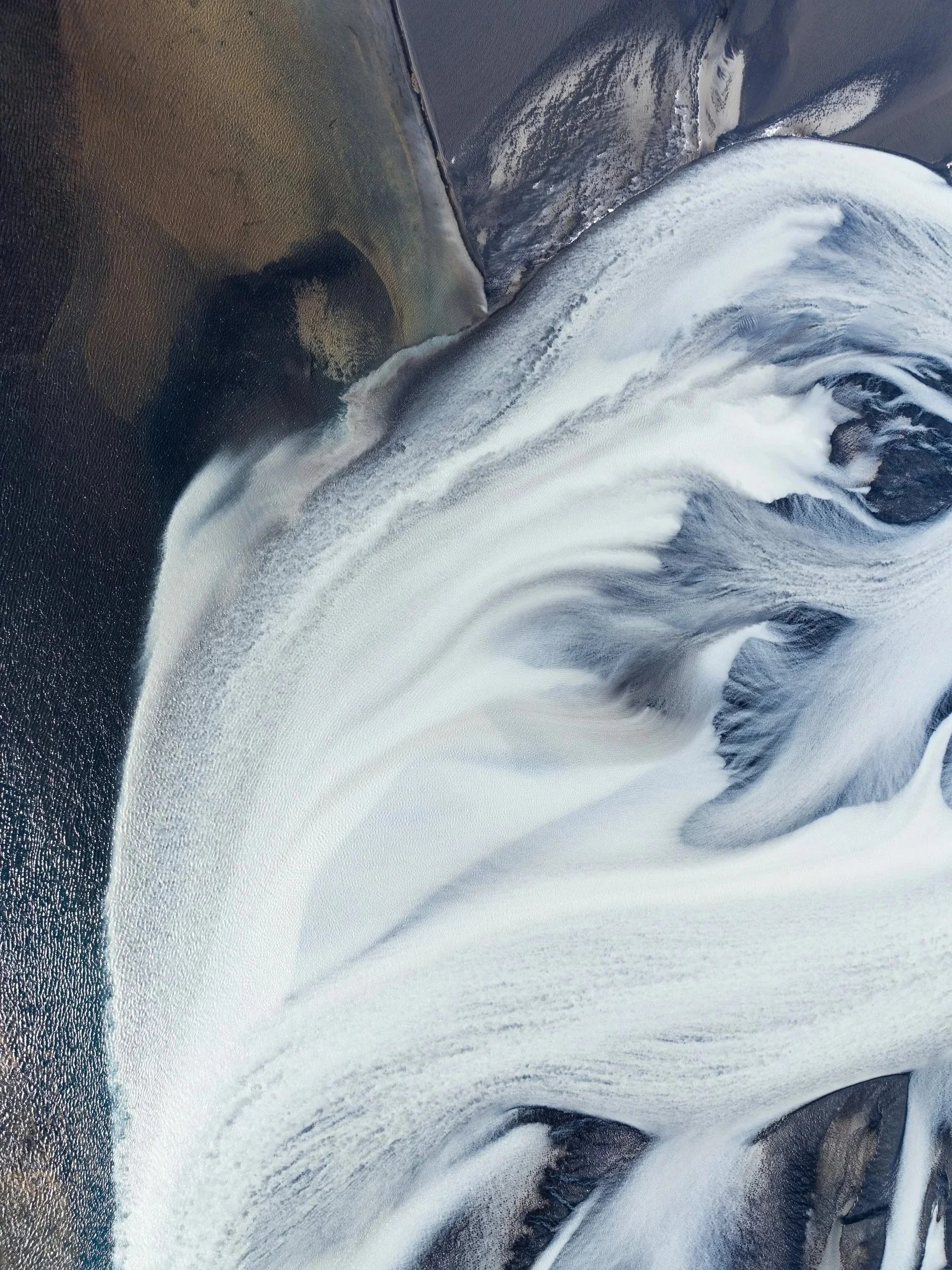 Aerial view of white glacier ice flowing around dark rock and sediment in Norway