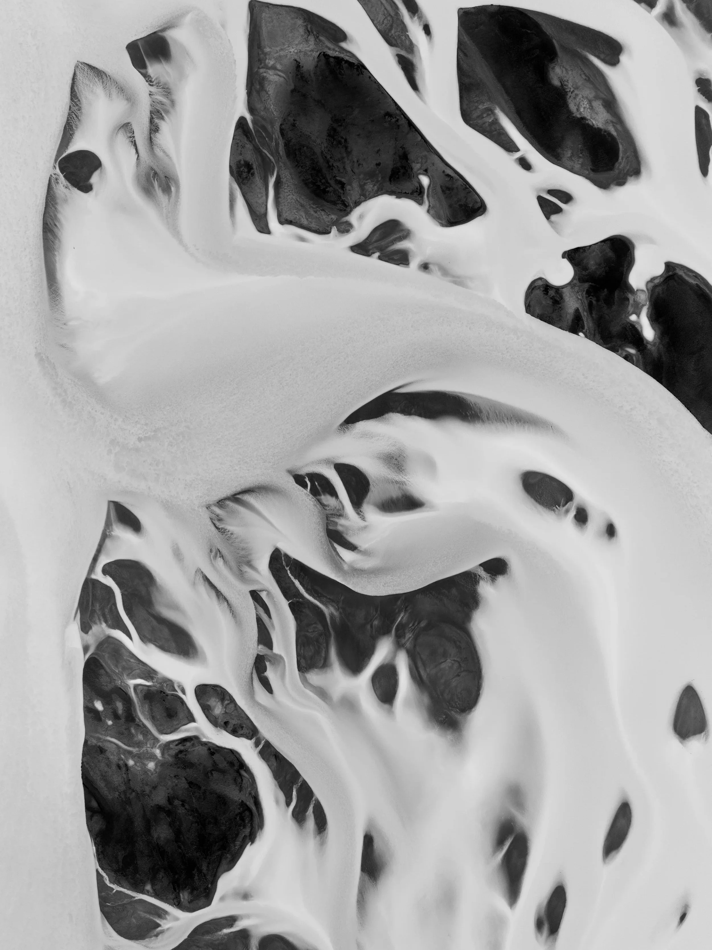 Aerial view of pale glacial water flowing through dark sediment in Iceland