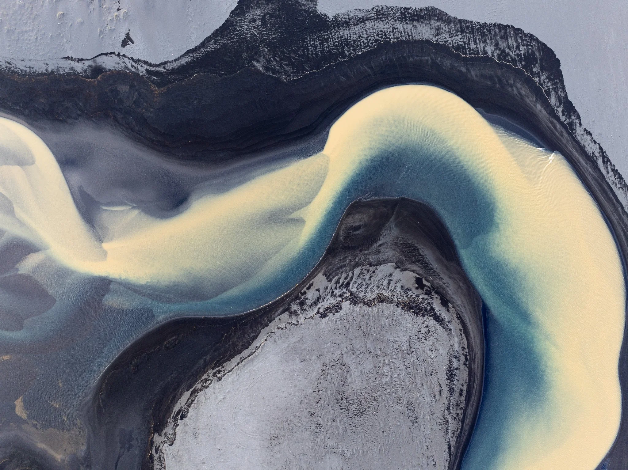Aerial view of a pale glacial river curving through dark volcanic terrain in Iceland