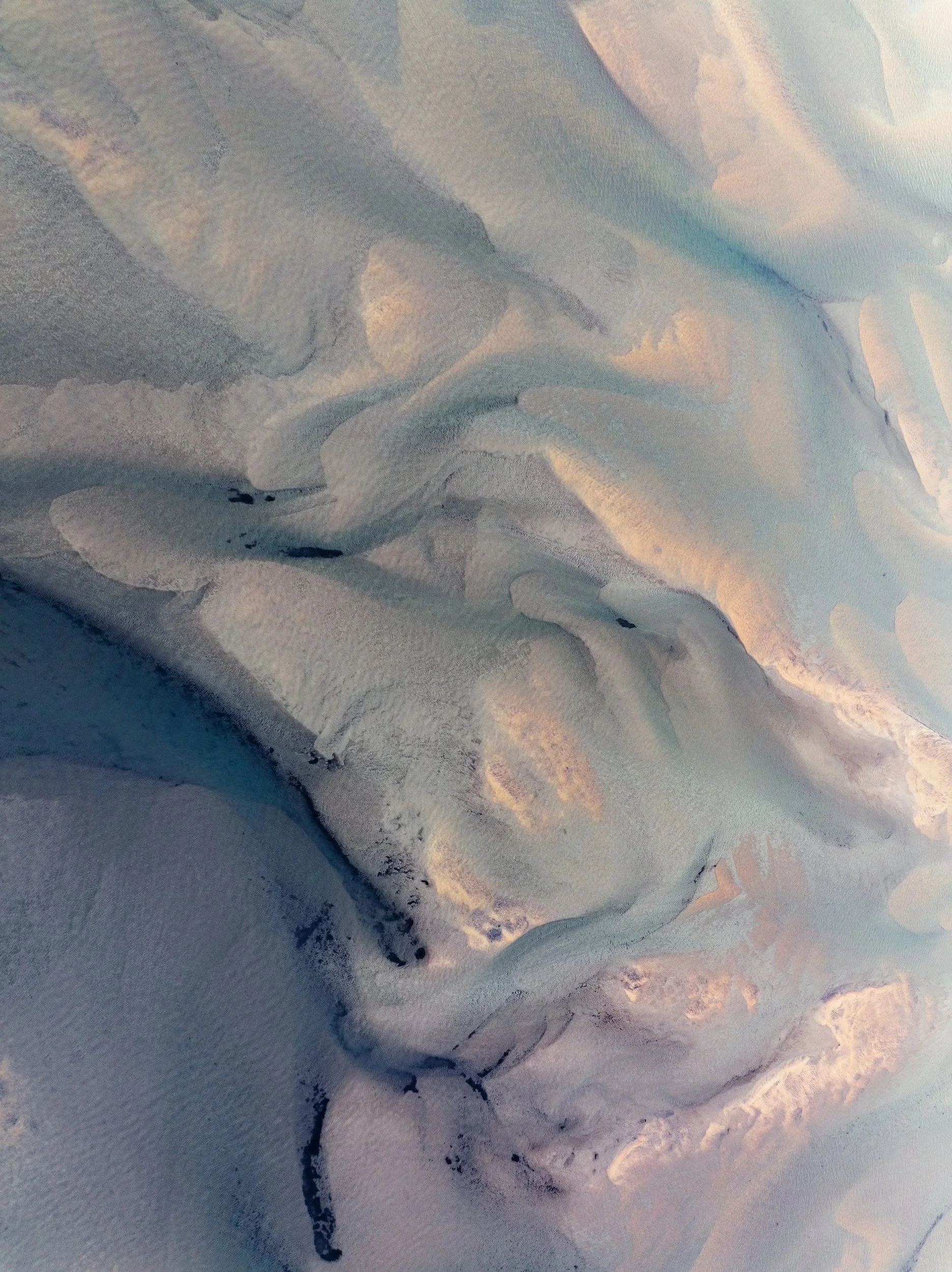 Aerial view of pale glacial water flowing through dark sediment in Iceland