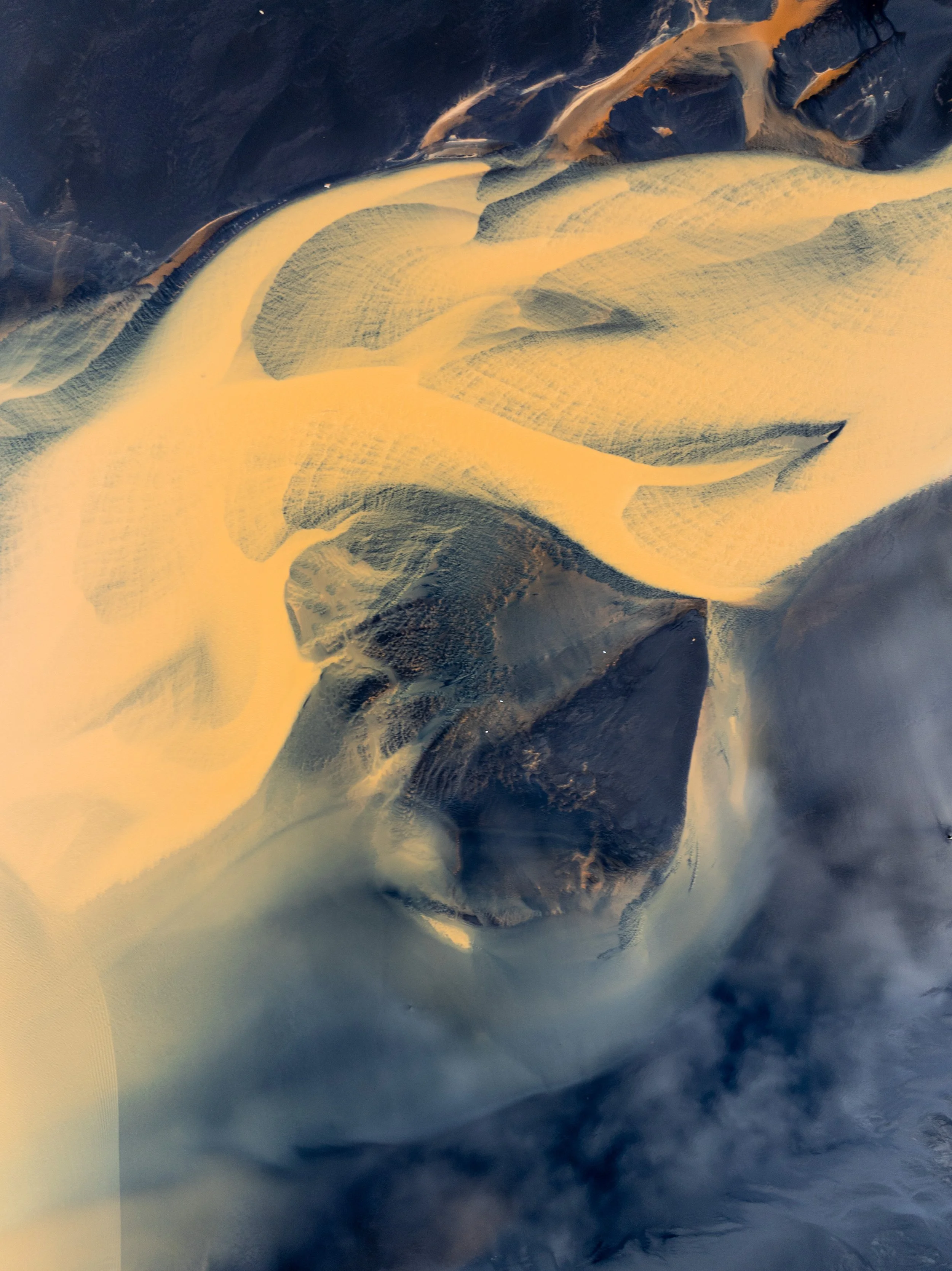 Aerial view of a glacial river and sediment patterns across dark volcanic terrain in Iceland