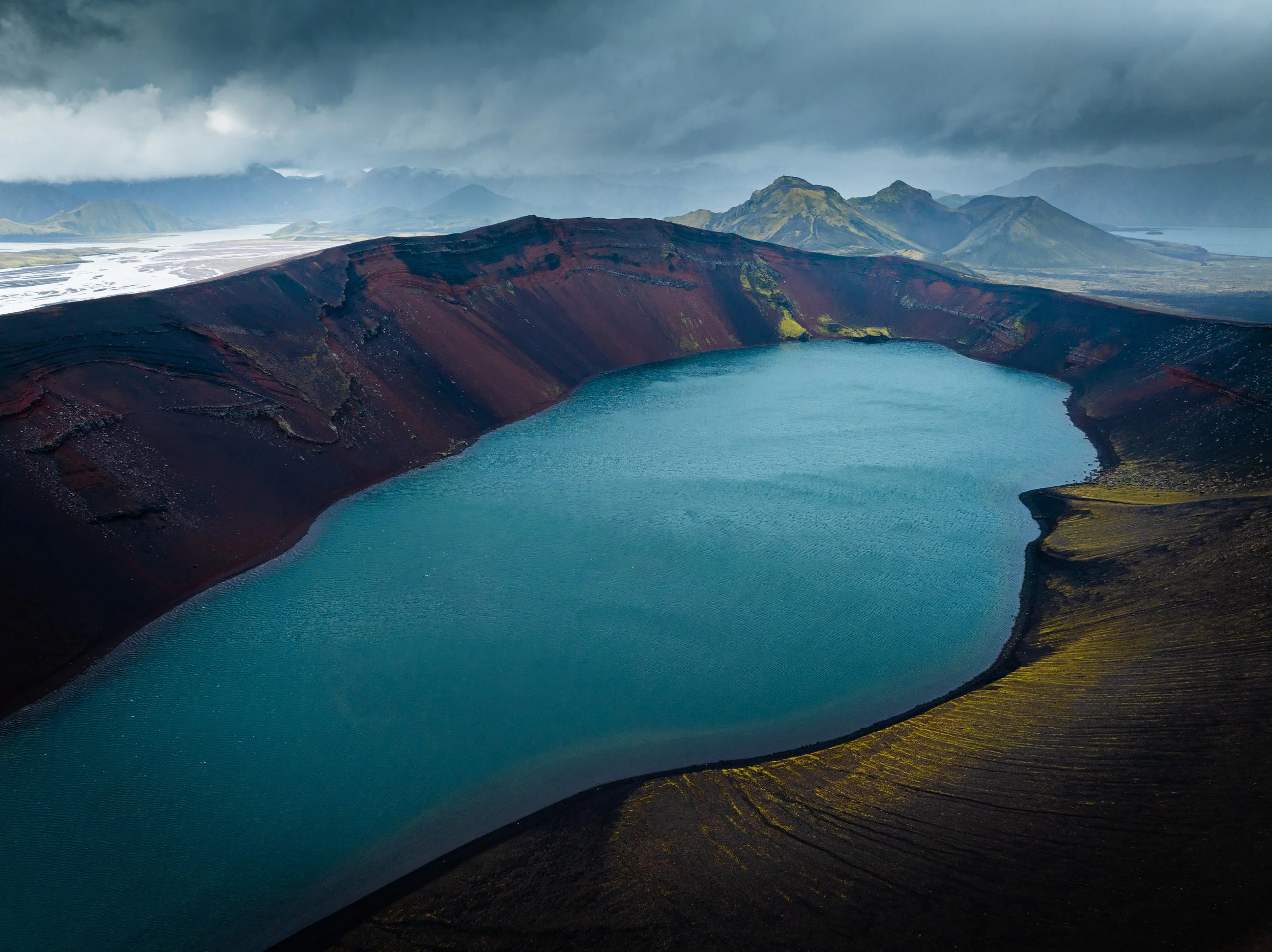 Turquoise crater lake surrounded by dark volcanic mountains in Bláhyllur, Iceland