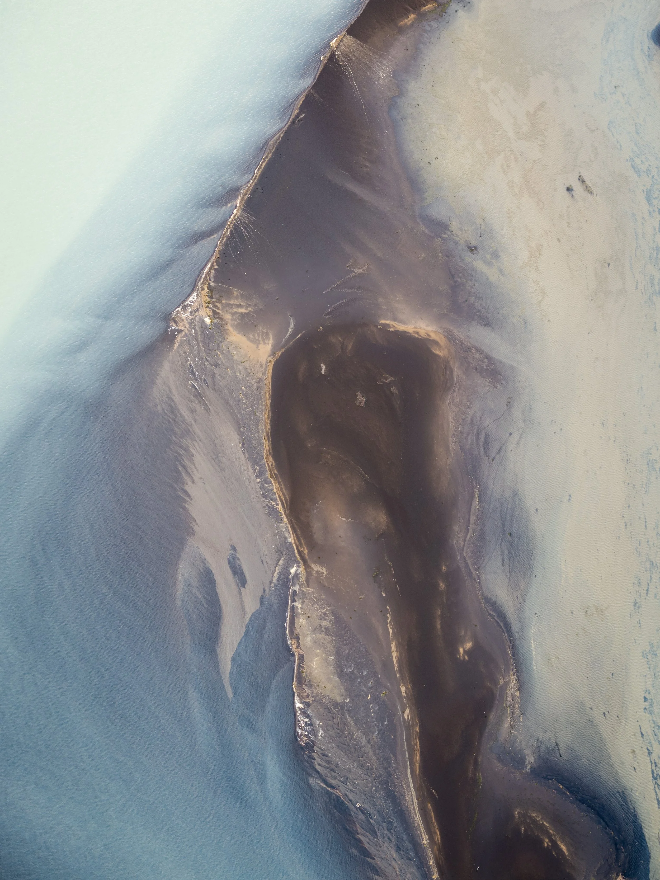 Aerial view of dark glacial sediment surrounded by pale mineral surfaces in Iceland