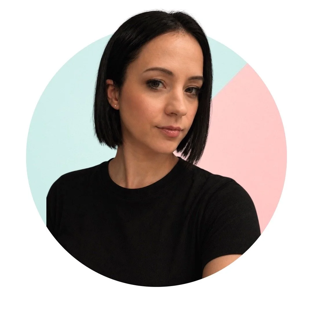 A woman with short black hair, wearing a black shirt, looking slightly to the right, with a pastel-colored background divided into light blue and pink sections.