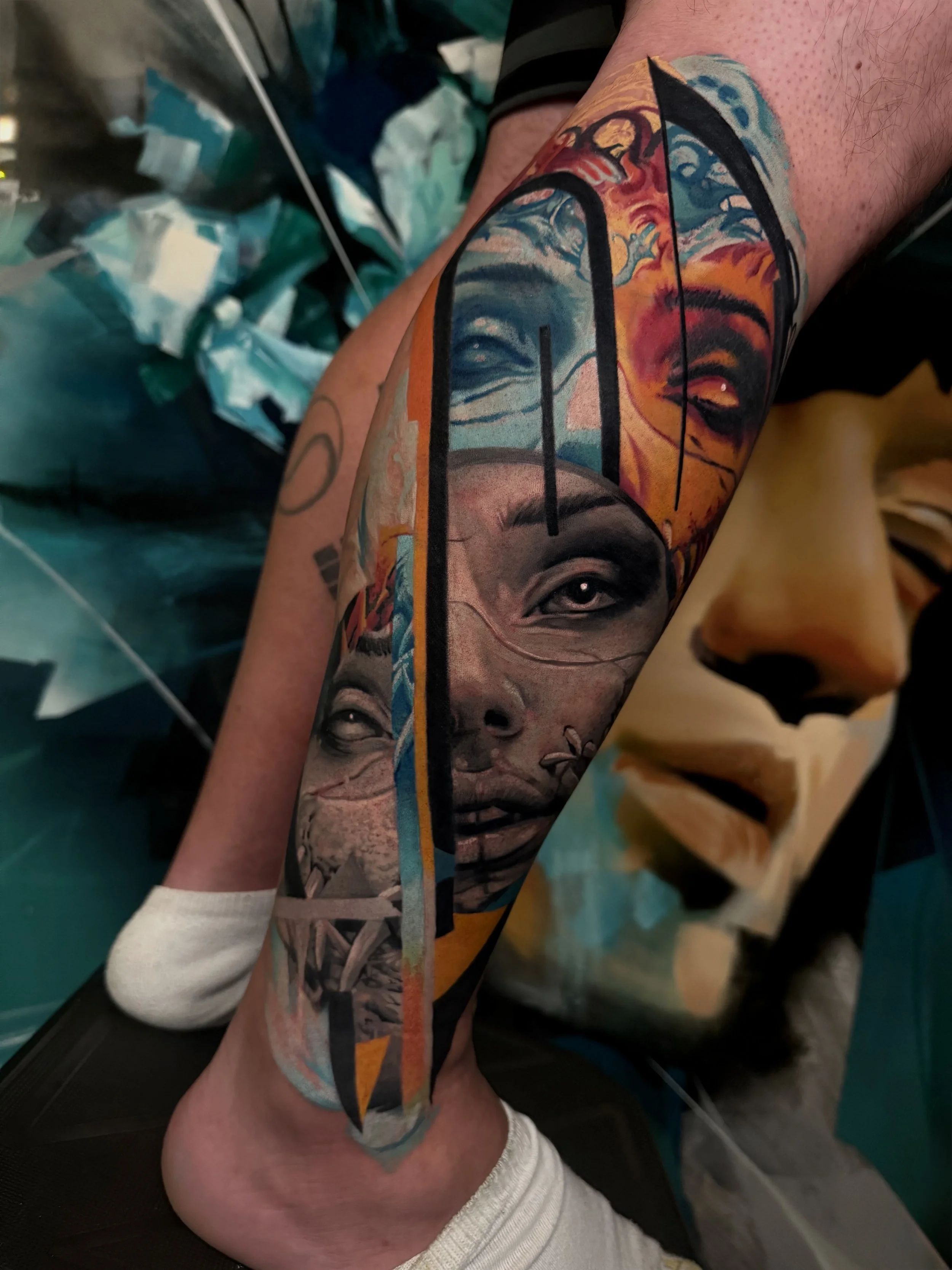 Close-up of a person's leg with a colorful tattoo of faces and abstract dark art.