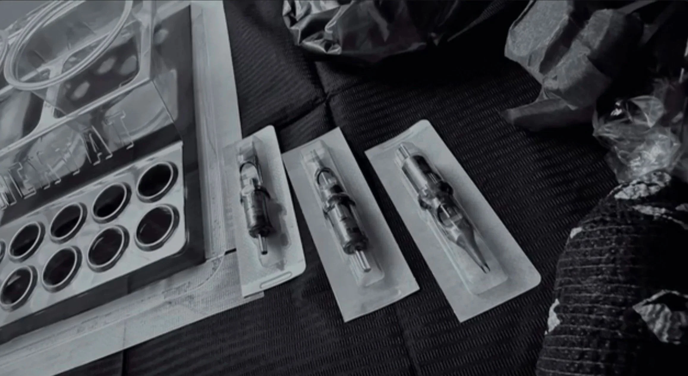 A variety of syringes and medical tools arranged on a surface, with some plastic packaging and black material around them.