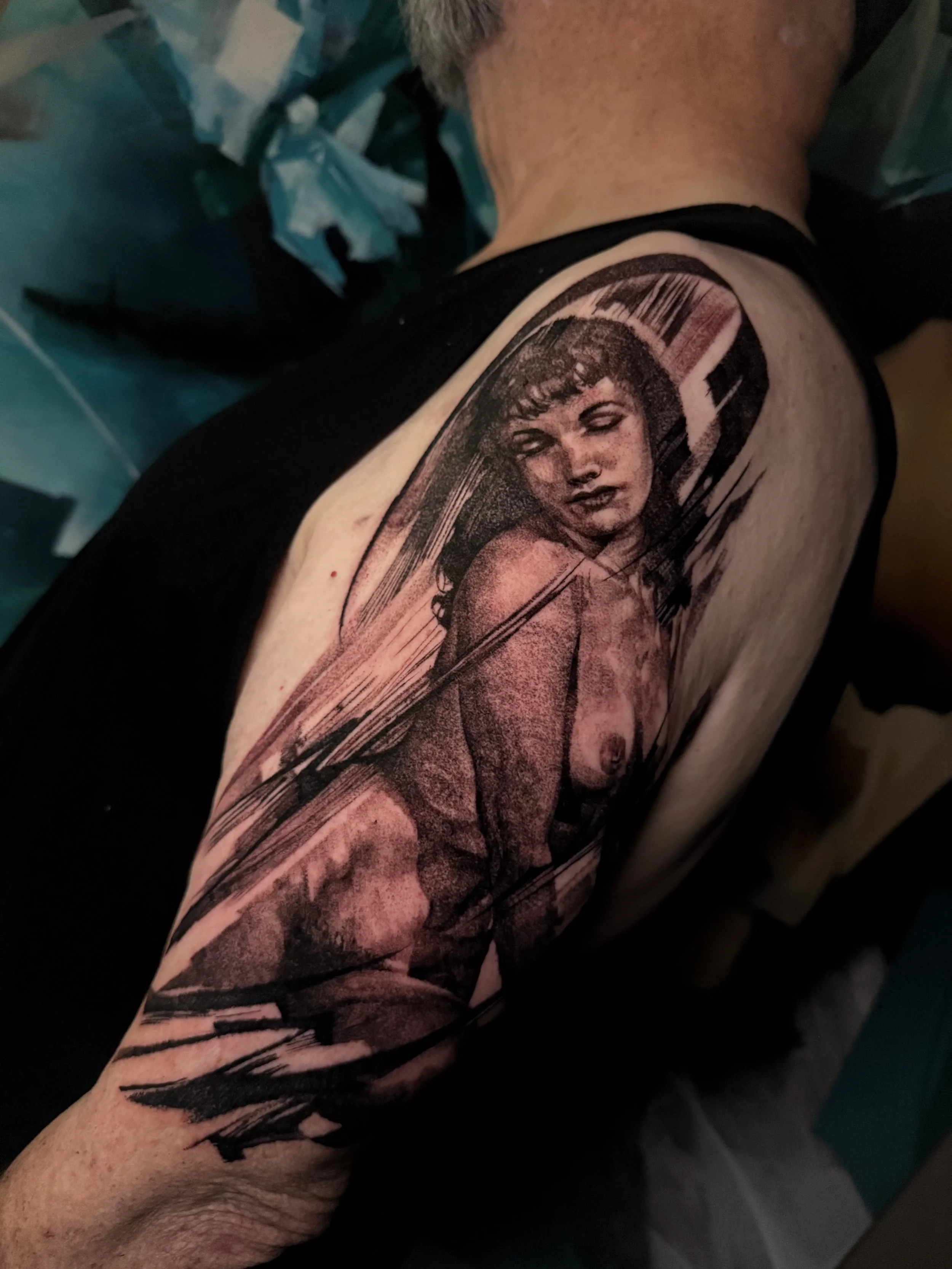 Tattoo of a woman's face with short hair and abstract markings on person’s upper arm.