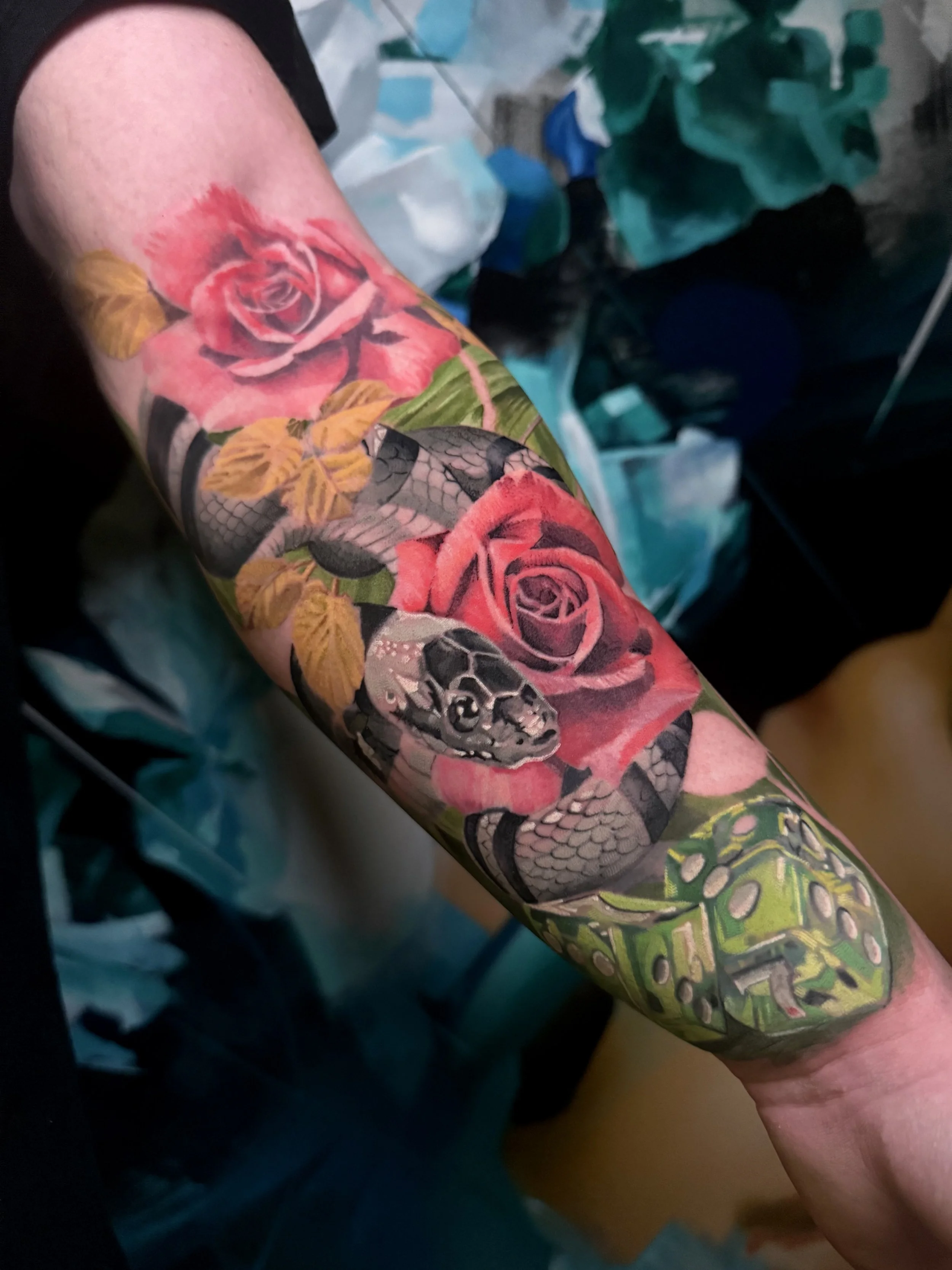 Tattoo sleeve featuring roses, a snake, and intricate designs on a person's arm.