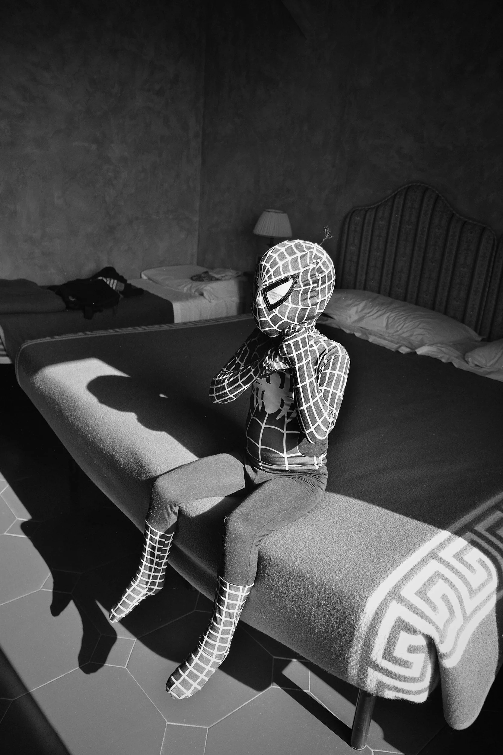A kid in his Spider-man costume, sitting on a bed waiting to save the day
