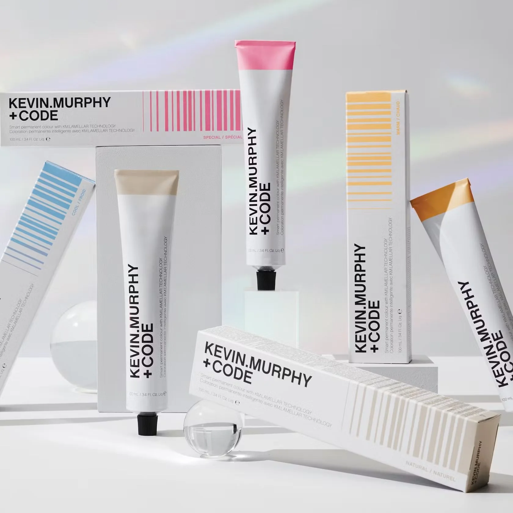 Multiple skincare products from Kevin Murphy + Code line, including tubes and boxes with branding in black, pink, yellow, and beige, displayed against a neutral background.