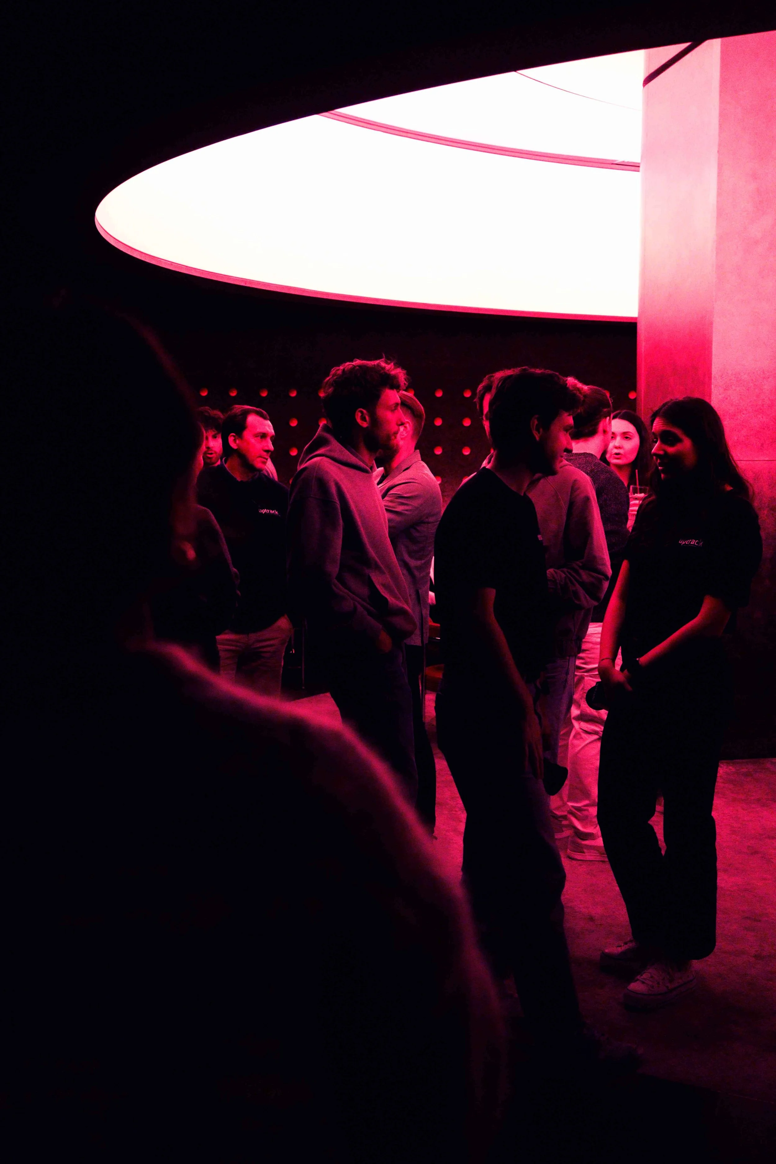 Foule de personnes réunies dans une salle sombre éclairée par une lumière rouge, sous un grand luminaire blanc (événement La Nuit du Trail).