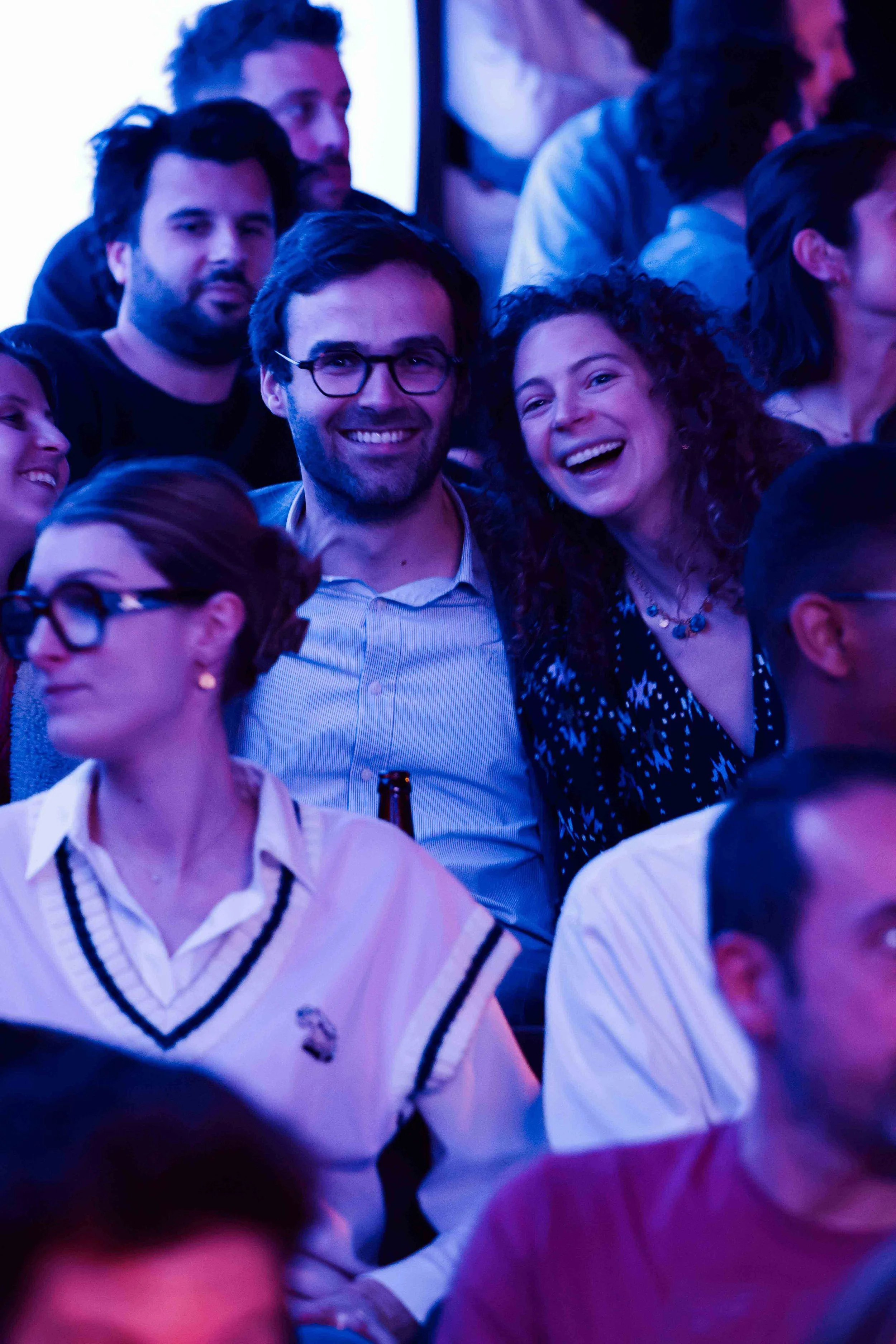Groupe de personnes souriantes réunies lors d’une soirée, sous un éclairage bleu et violet (événement La Nuit du Trail).