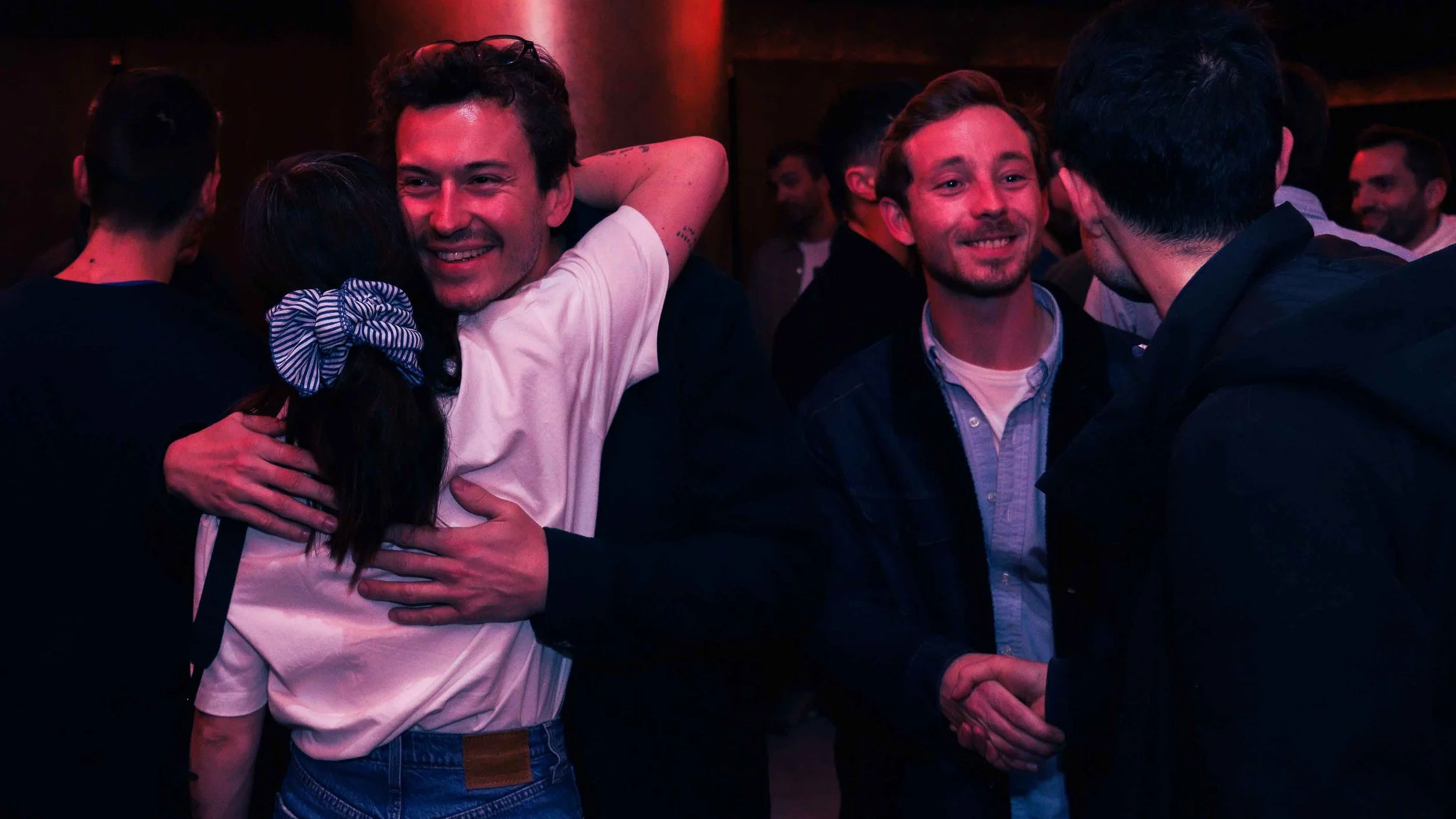 Groupe d’amis souriants se retrouvant dans une soirée éclairée de lumières rouges (événement La Nuit du Trail).
