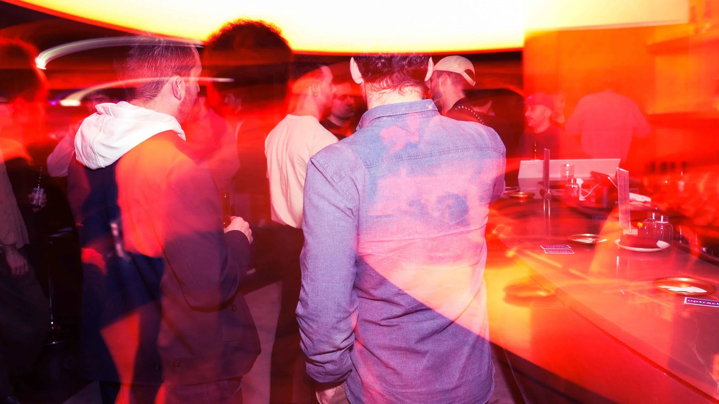 Foule dans un bar ou une boîte de nuit, éclairée par des lumières rouges, près d’un comptoir (événement La Nuit du Trail).