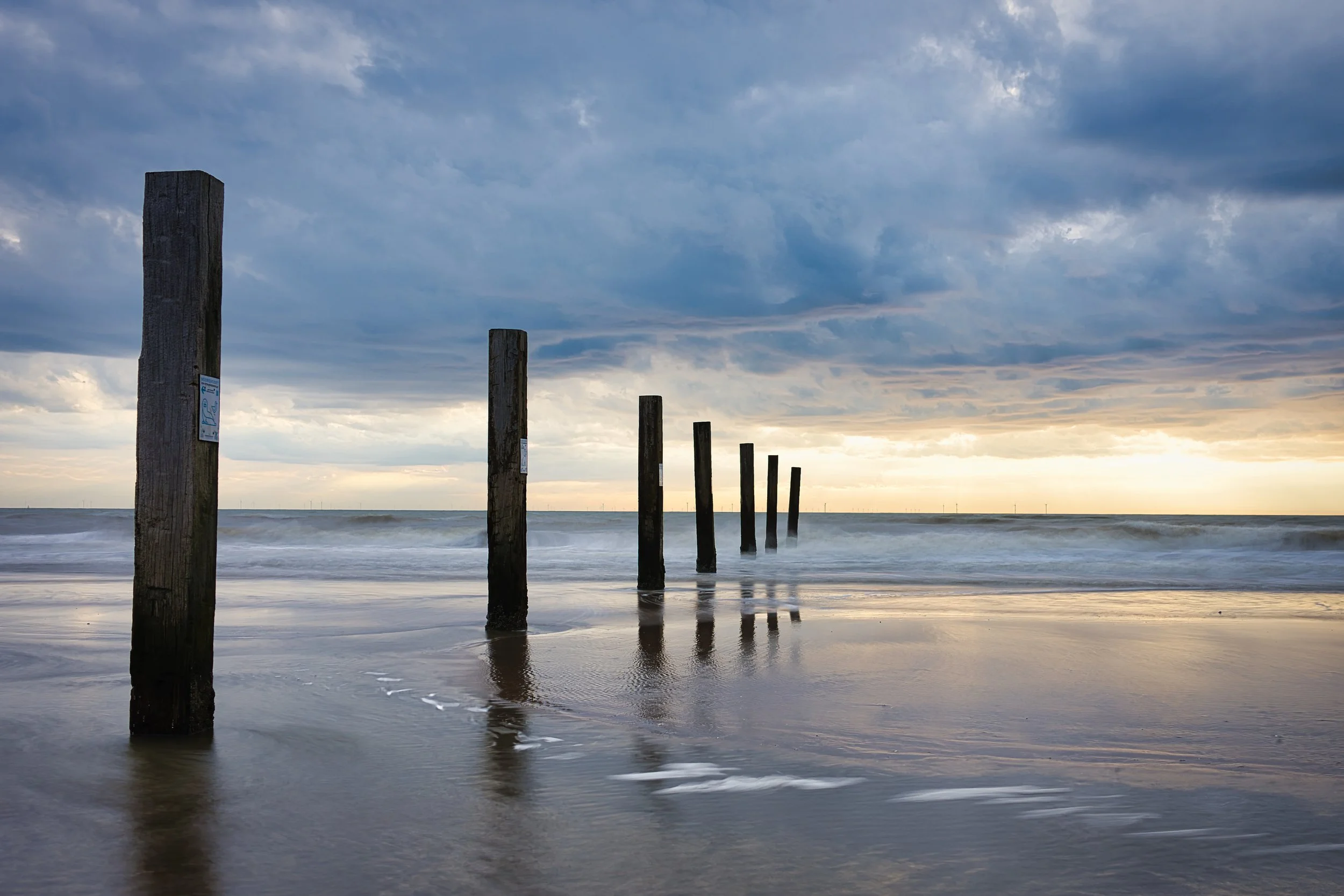 Houten steigerpalen in de zee met een bewolkte hemel.