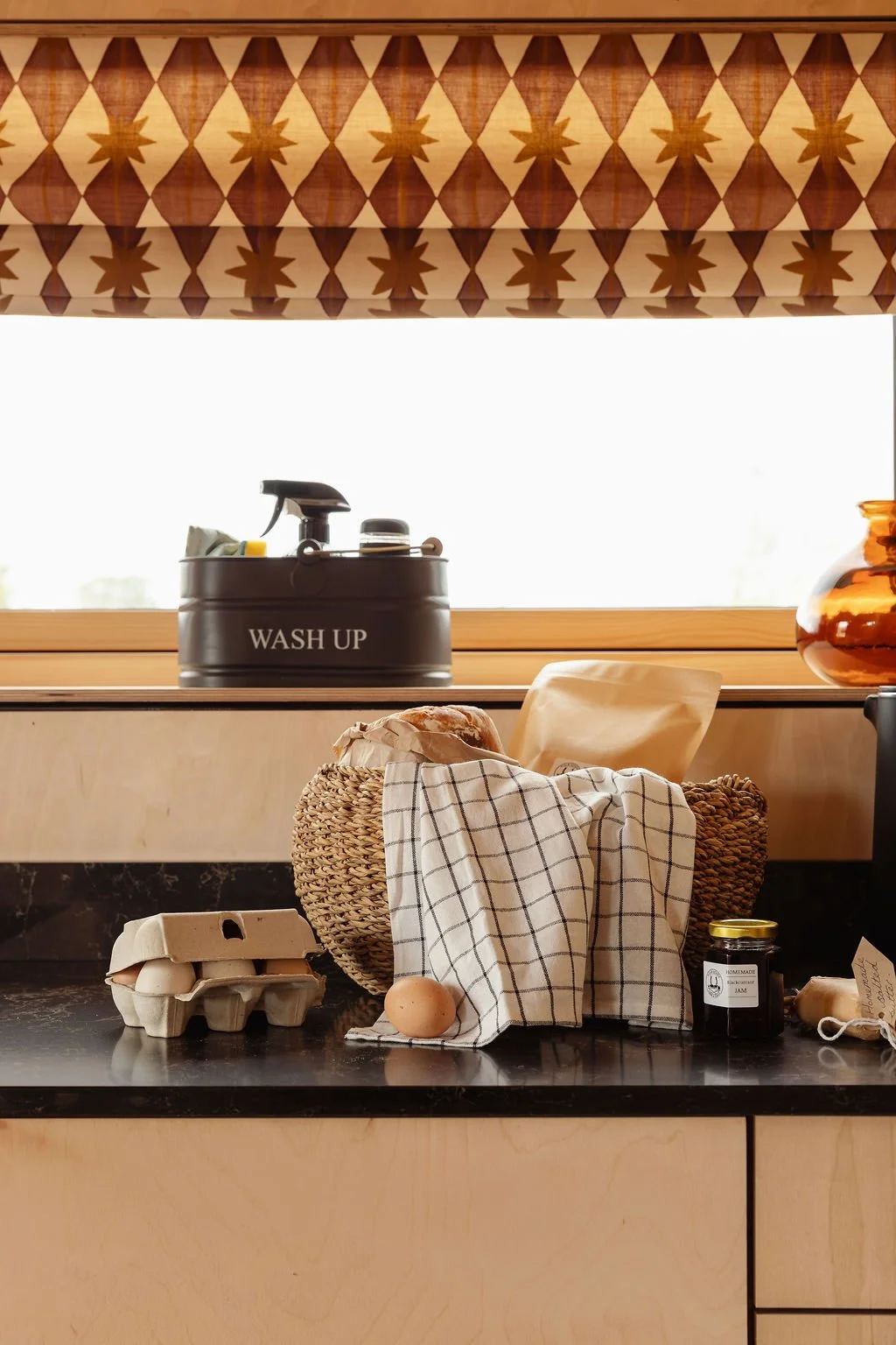 Handmade ply kitchen with black worksurfaces and a breakfast basket on top. Ashleigh Mercia blind.