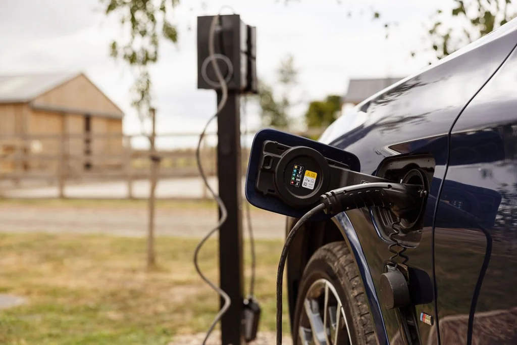 Electric vehicle being charged at an outdoor charging station, with a house and trees in the background.