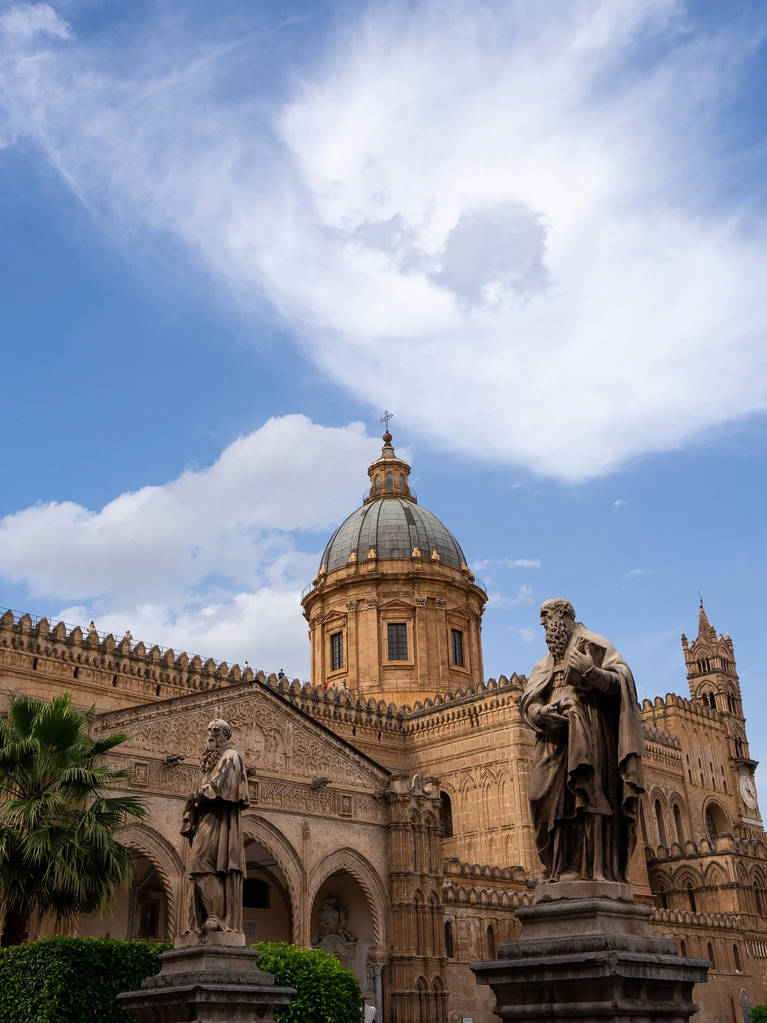 Statues of religious figures and architectural elements in a historic building with a large dome, set against a blue sky with clouds.